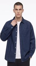 A man wearing a dark blue denim button-up shirt over a white t-shirt and black pants, photographed against a clean white studio background, from Meleche Fashion USA or Meléche (short as (Mé))