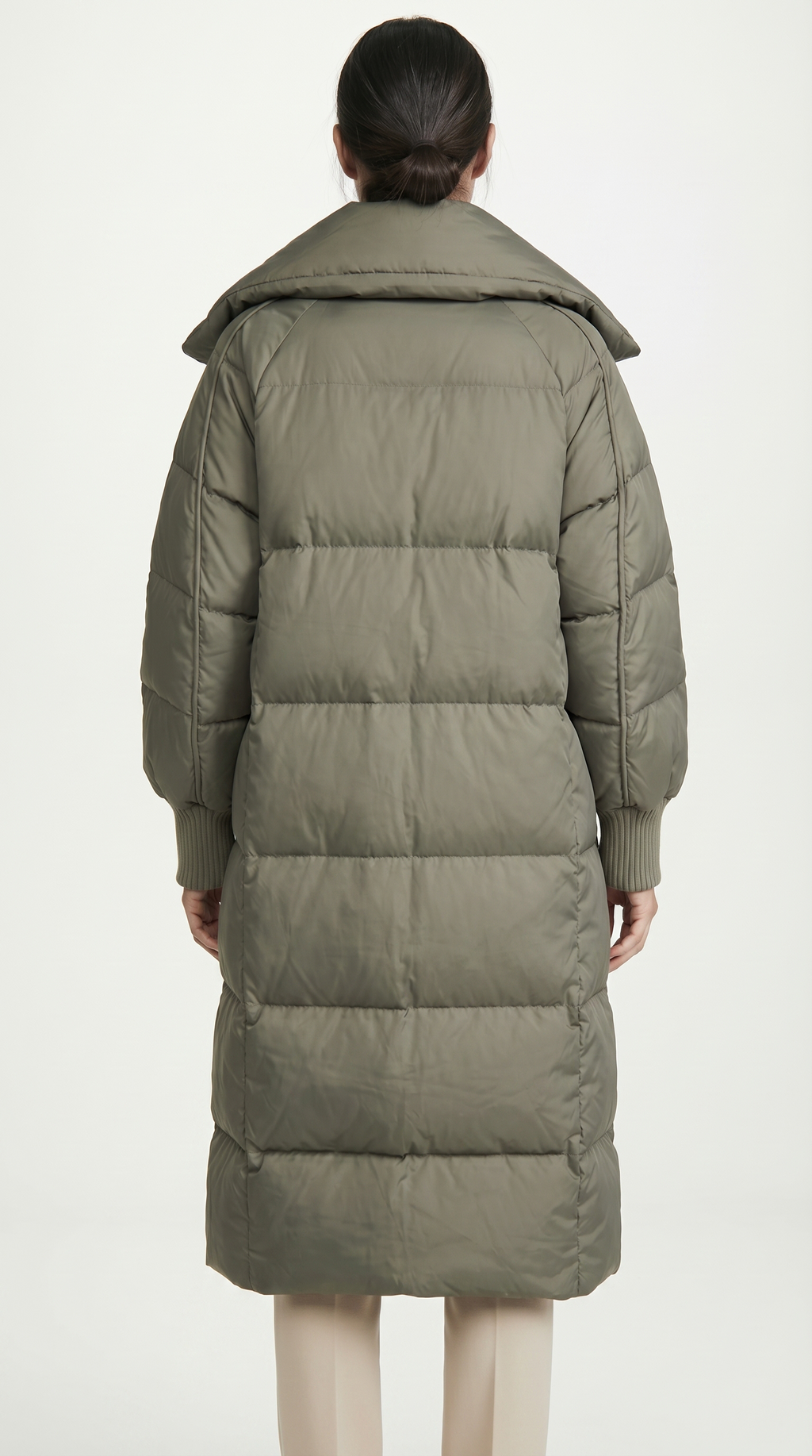 Person wearing a long olive green puffer coat on a white background from Meleche USA or Meléche (short as (Mé))