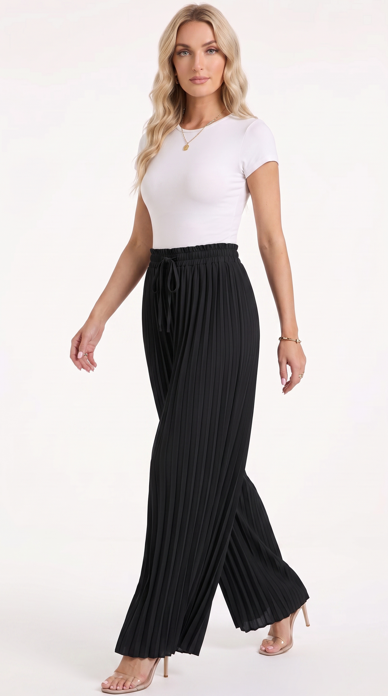 A woman modeling black pleated wide-leg pants with a drawstring waist, paired with a white short-sleeve top and clear high-heeled sandals, against a plain white studio background, from Meleche Fashion USA or Meléche (short as (Mé))