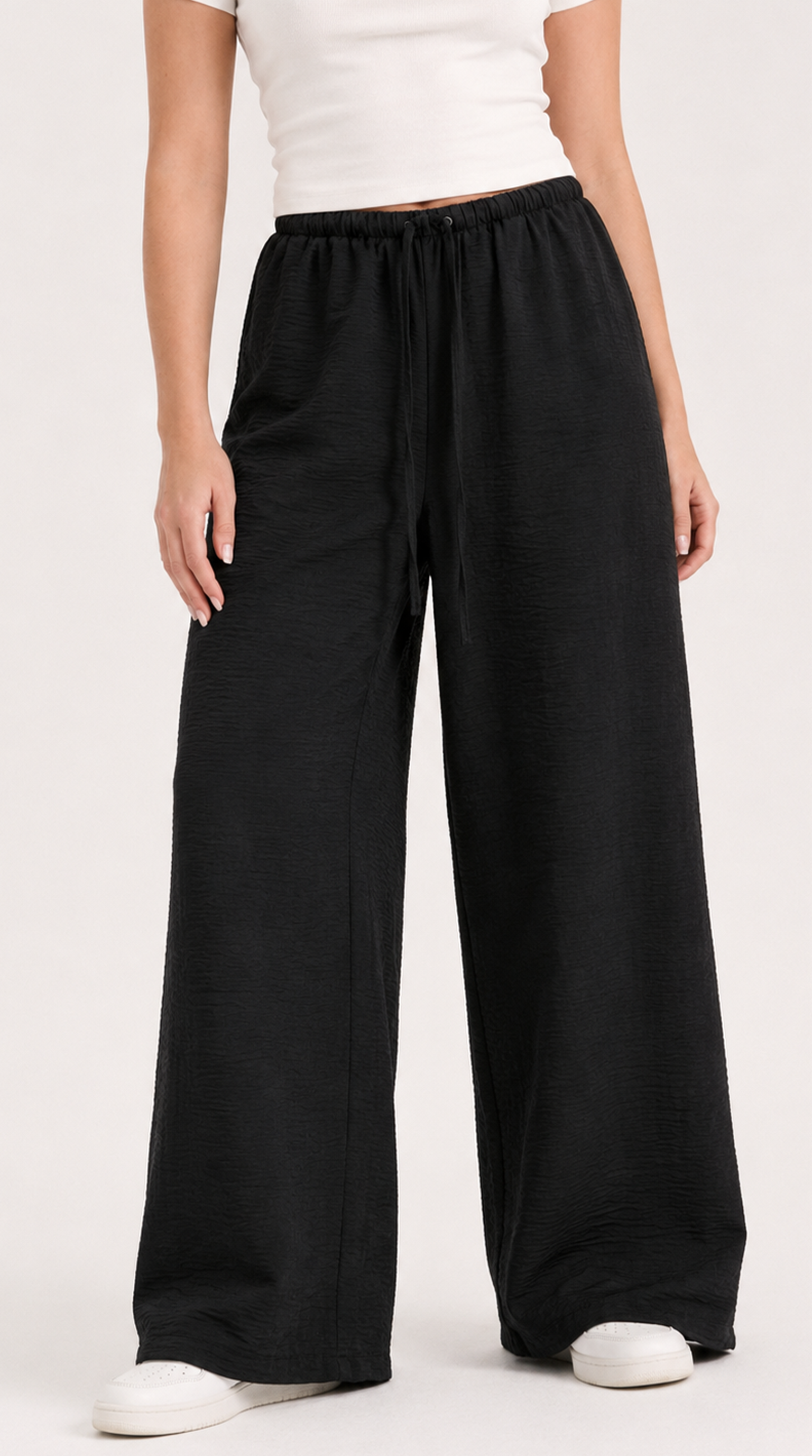 Person wearing black wide-leg pants and a white top on a plain background, from Meleche Fashion USA or Meléche (short as (Mé))