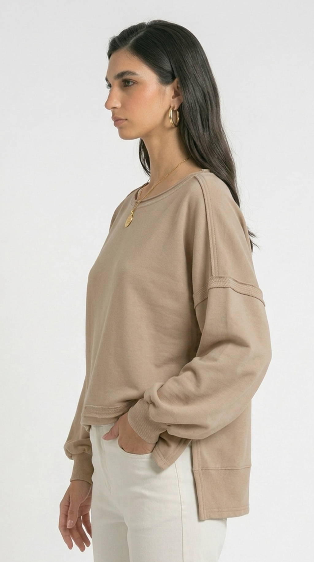 Woman wearing a beige long-sleeve top and white pants on a white background