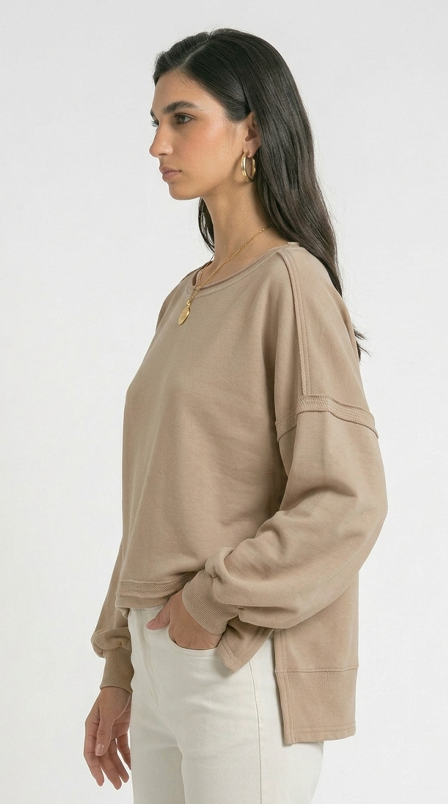Woman wearing a beige long-sleeve top and white pants on a white background
