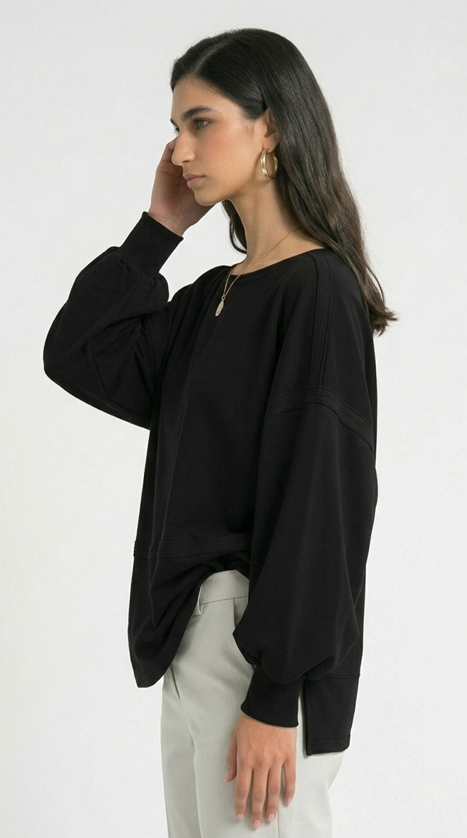 Woman wearing a black oversized sweater and white pants on a white background