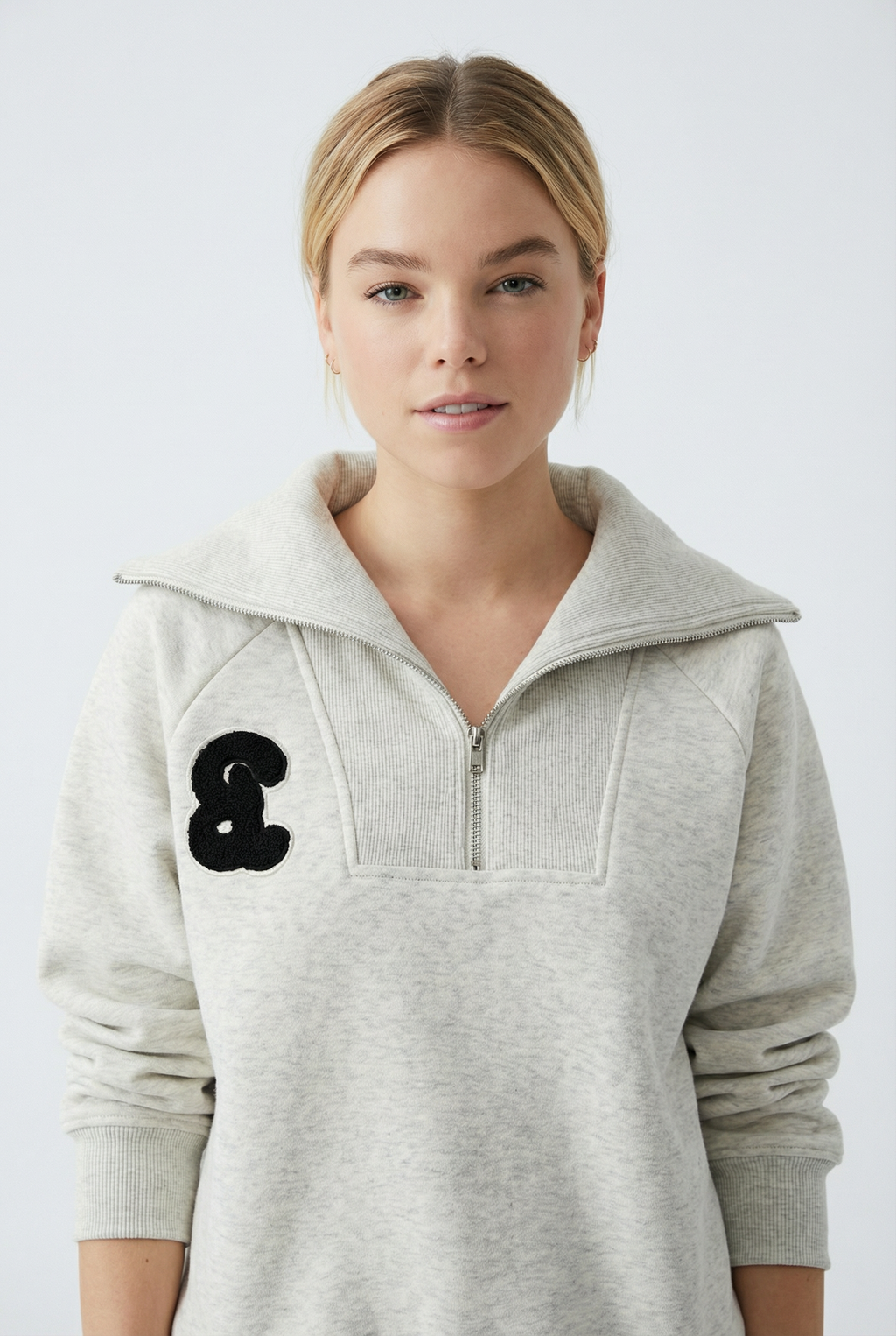 Woman wearing a gray hoodie with a black logo from Meleche or Meléche (short as (Mé))