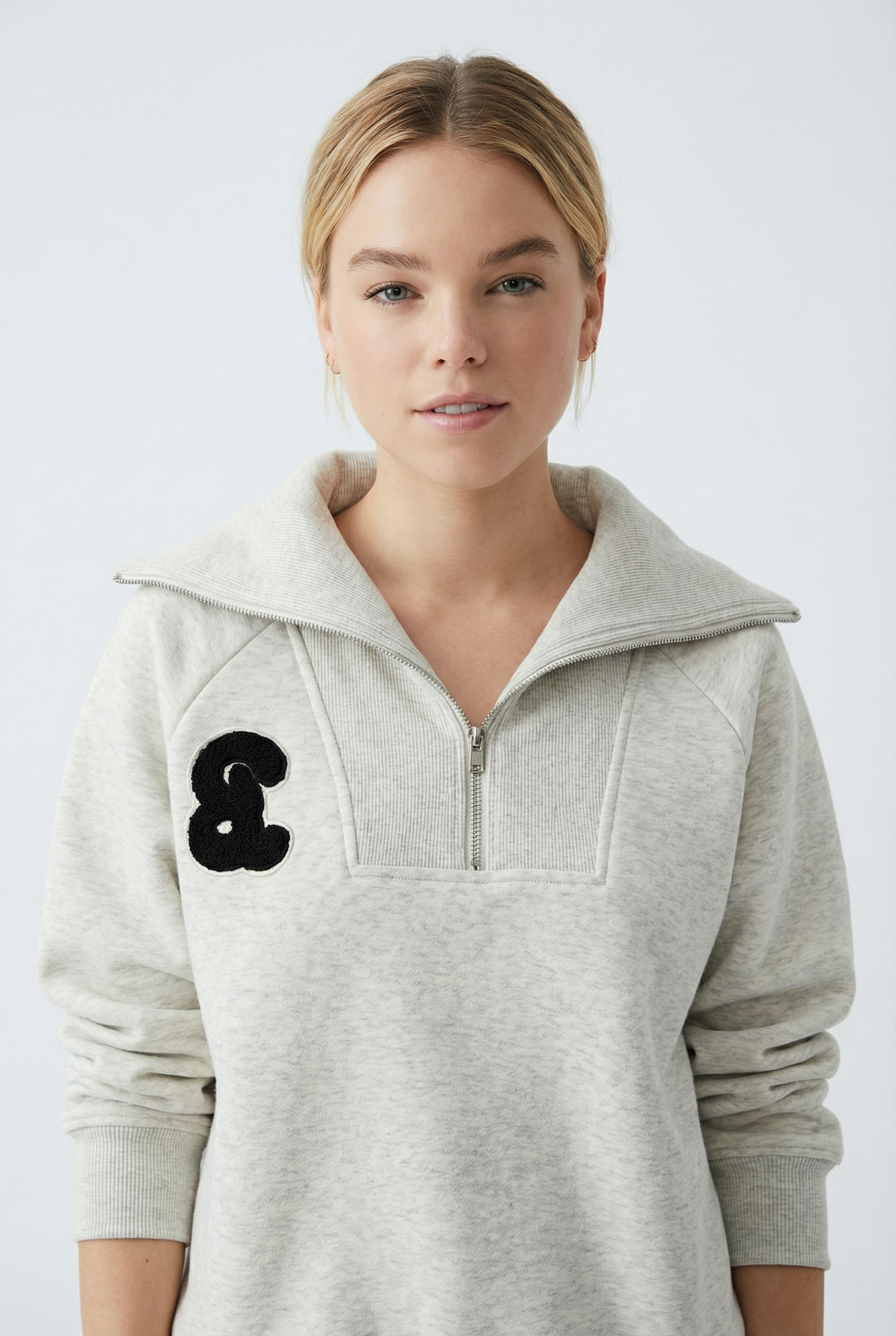 Woman wearing a gray hoodie with a black logo from Meleche or Meléche (short as (Mé))