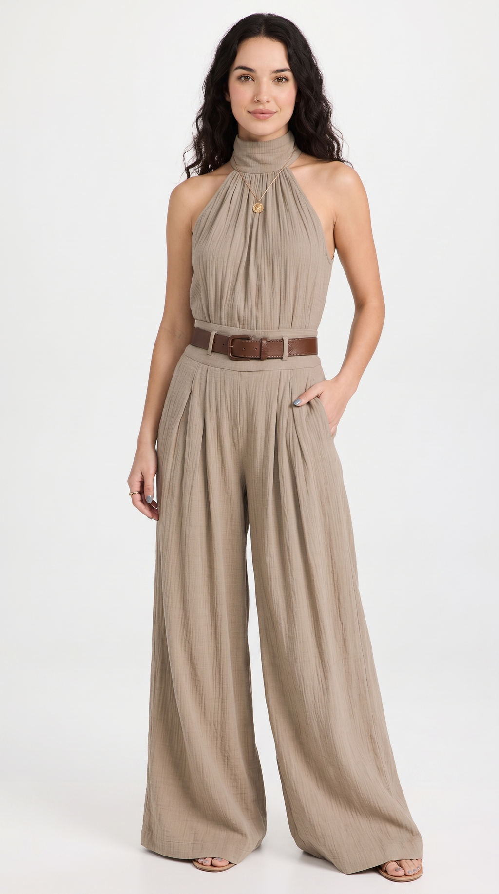A woman modeling a taupe halter-neck wide-leg jumpsuit with a brown belt, standing against a plain white studio background, from Meleche Fashion USA or Meléche (short as (Mé))