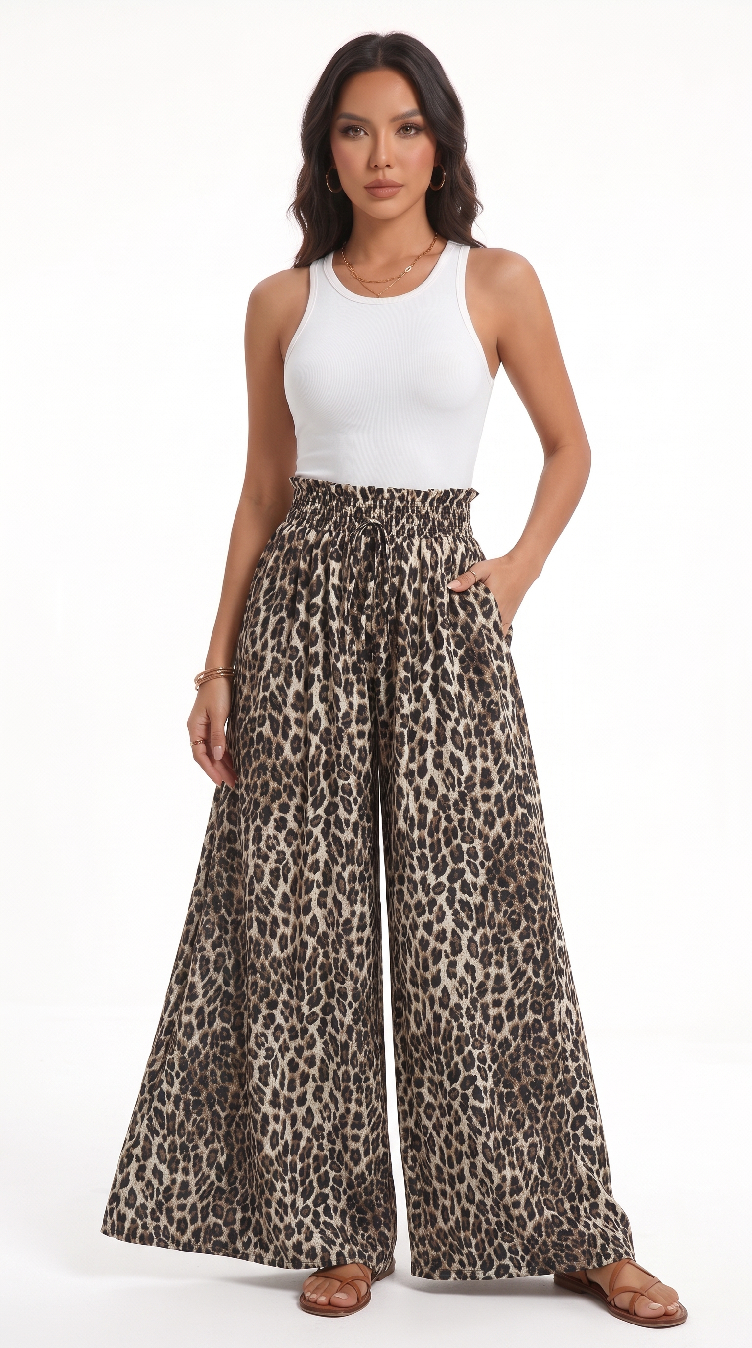 A woman modeling a pair of high-waisted, wide-leg pants with a brown and black leopard print pattern, paired with a white tank top and brown sandals, against a plain white studio background, from Meleche Fashion USA or Meléche (short as (Mé))