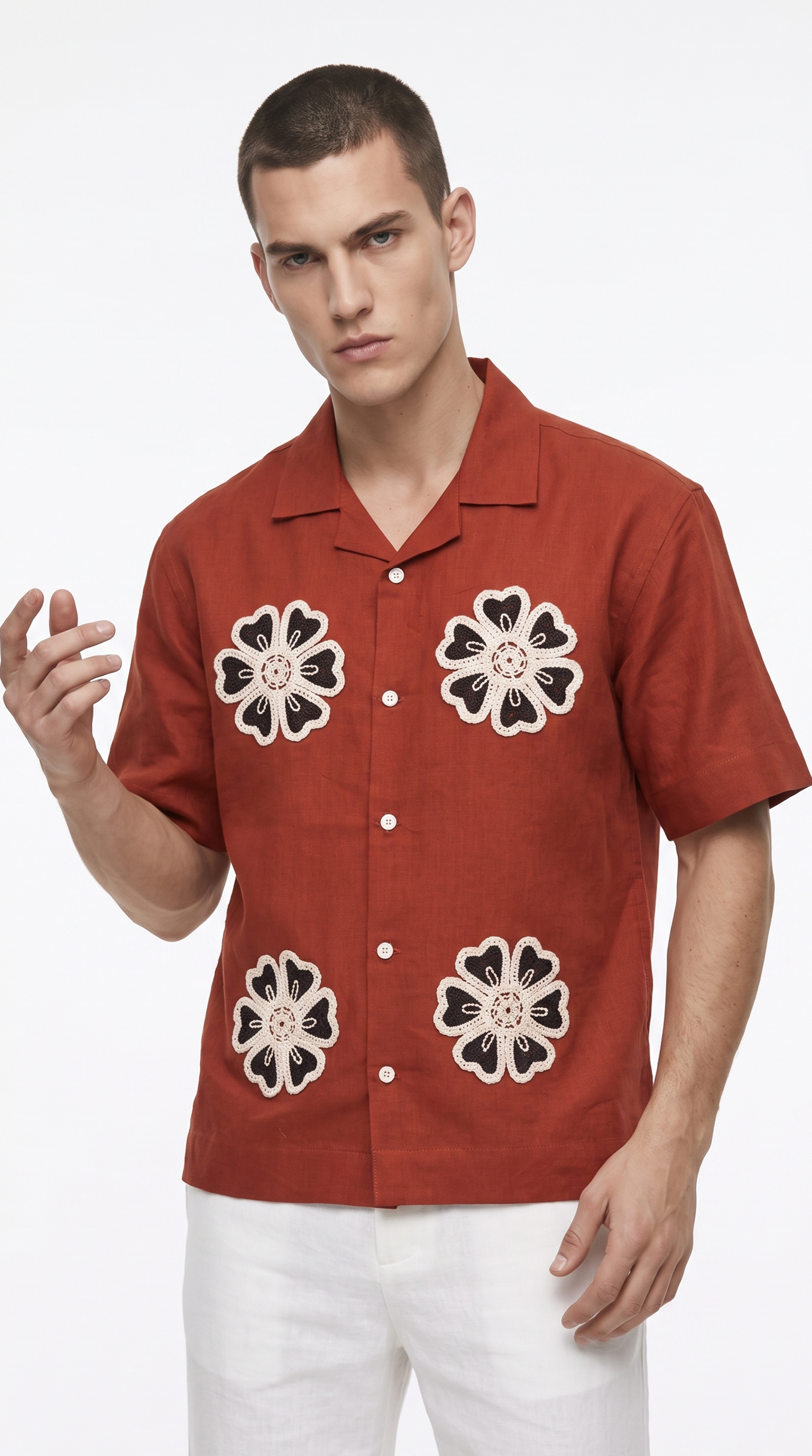 A man wearing a rust-orange short-sleeve button-up shirt with three large black and beige floral embroidered motifs on the front, paired with white pants, against a plain white background, from Meleche Fashion USA or Meléche (short as (Mé))