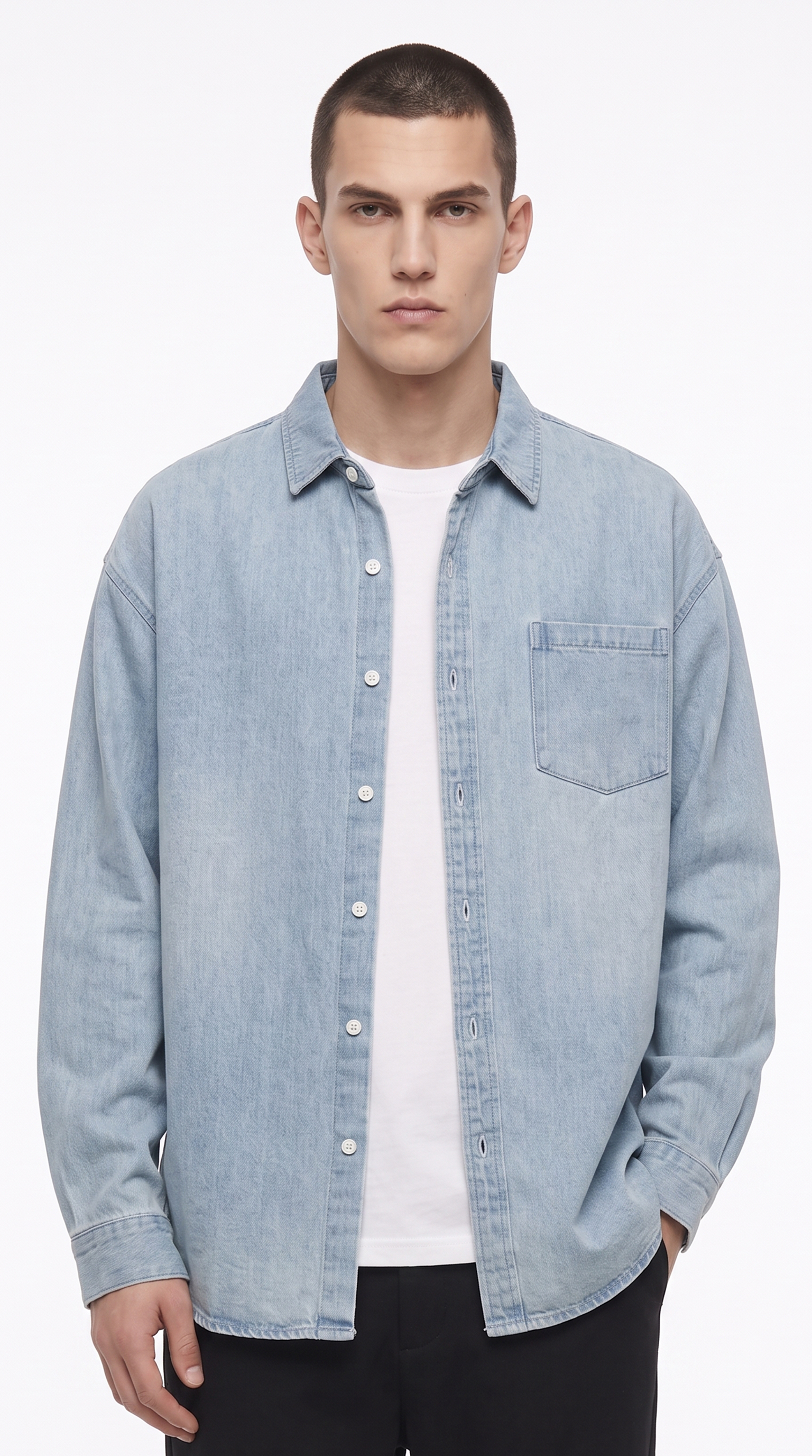 A male model wearing a light blue denim button-up shirt over a white t-shirt and black pants, photographed against a clean white studio background, from Meleche Fashion USA or Meléche (short as (Mé))