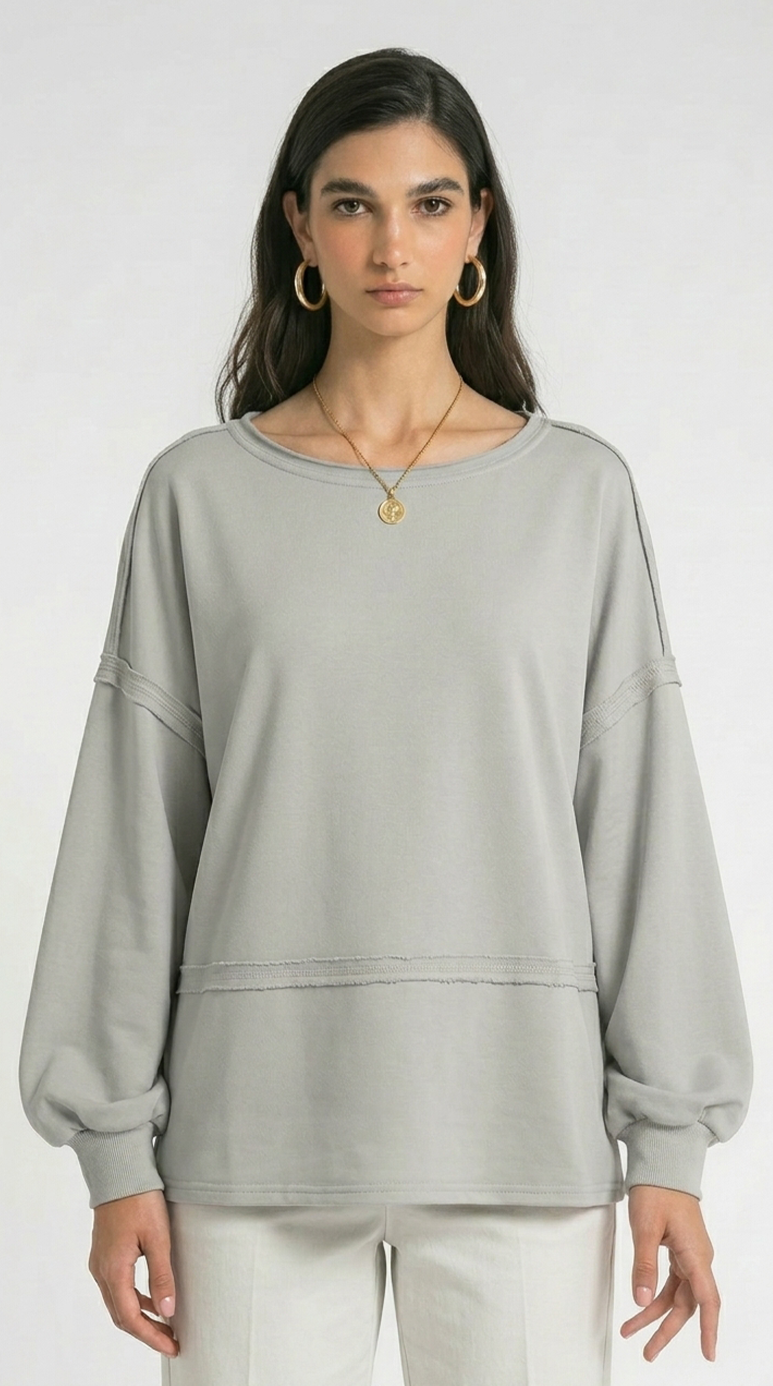 Woman wearing a light gray sweatshirt and white pants on a white background