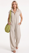 A woman modeling a light beige linen jumpsuit with a front zipper and wide legs, carrying a lime green shoulder bag against a white studio background, from Meleche Fashion USA or Meléche (short as (Mé))