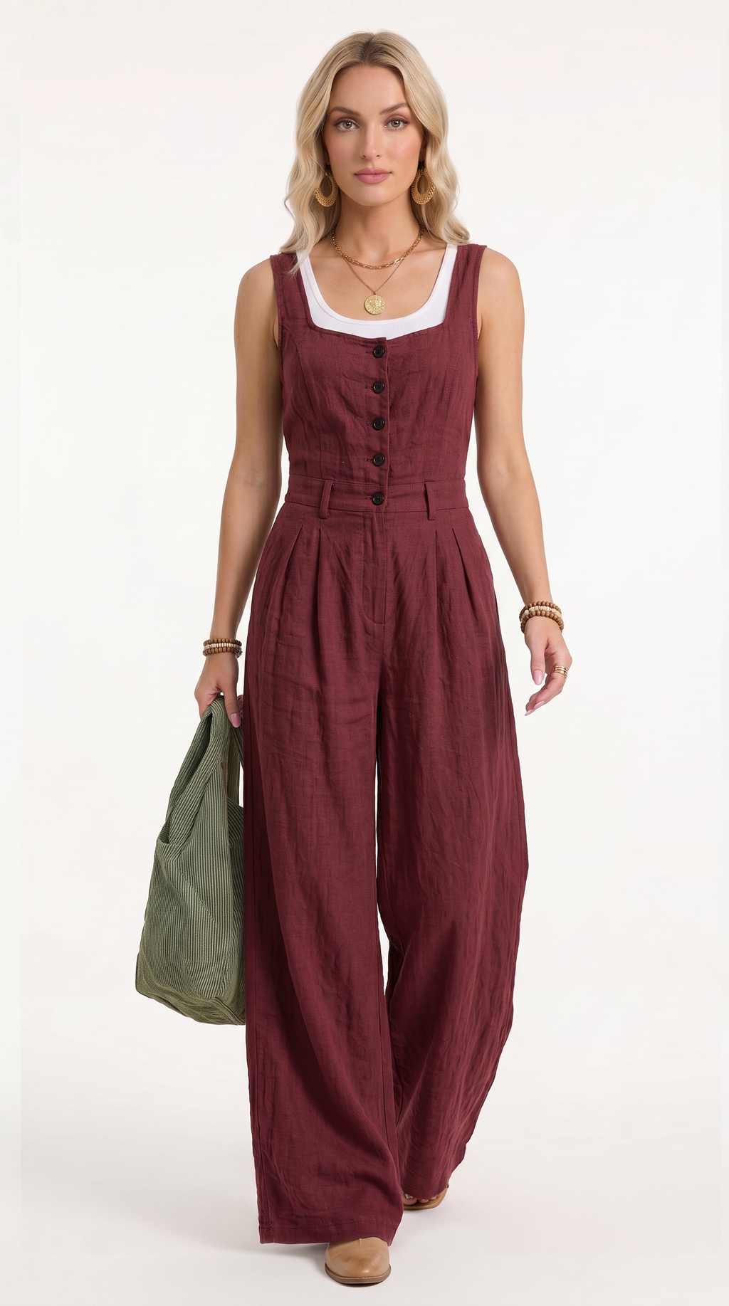 A woman modeling a sleeveless burgundy wide-leg jumpsuit with a white scoop neck insert and front buttons, holding an olive green tote bag against a plain white studio background.