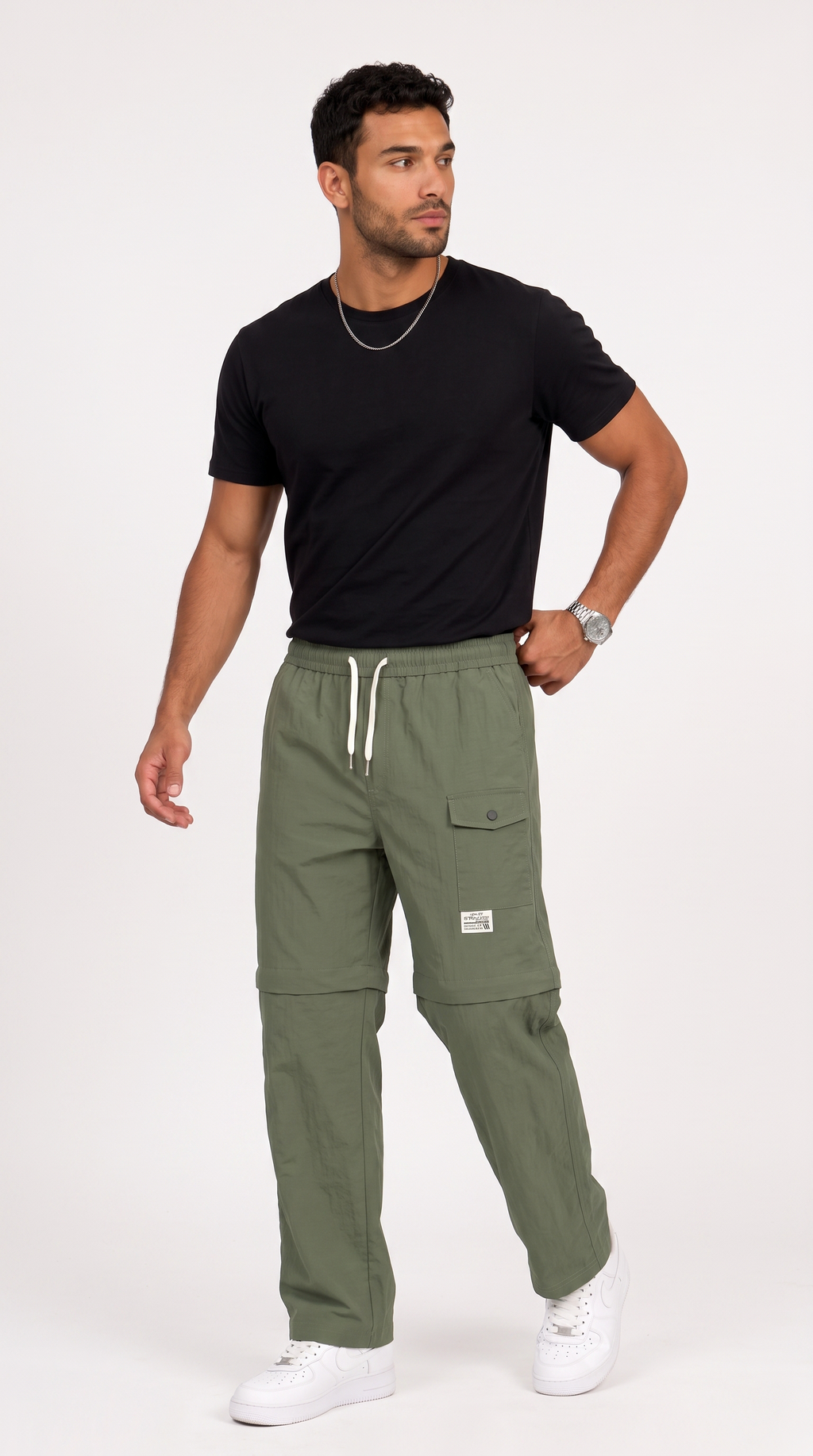 A man modeling olive green cargo pants with a black t-shirt and white sneakers, standing against a light gray studio background, from Meleche Fashion USA or Meléche (short as (Mé))