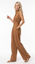 A woman modeling a sleeveless, high-neck, wide-leg jumpsuit in a warm camel brown color, standing against a plain white studio background, from Meleche Fashion USA or Meléche (short as (Mé))