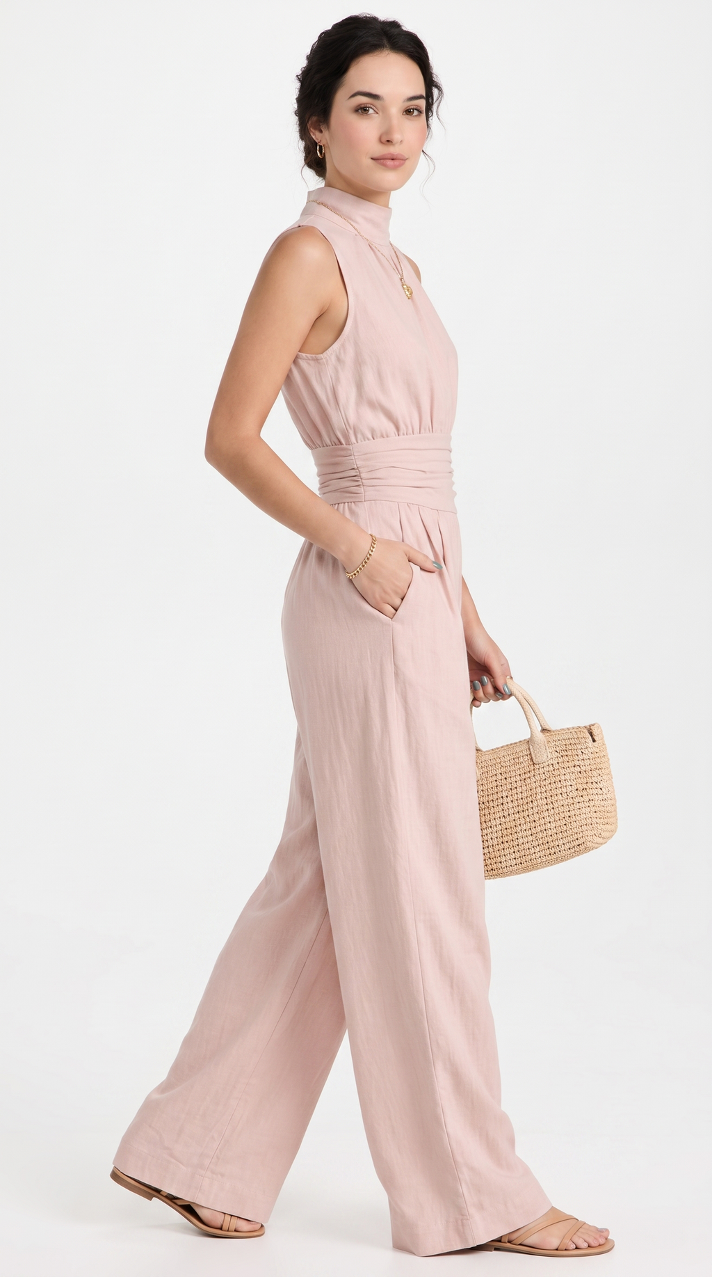 A woman modeling a sleeveless dusty pink wide-leg jumpsuit with a gathered waist, paired with a woven straw handbag and flat sandals, against a plain white studio background, from Meleche Fashion USA or Meléche (short as (Mé))