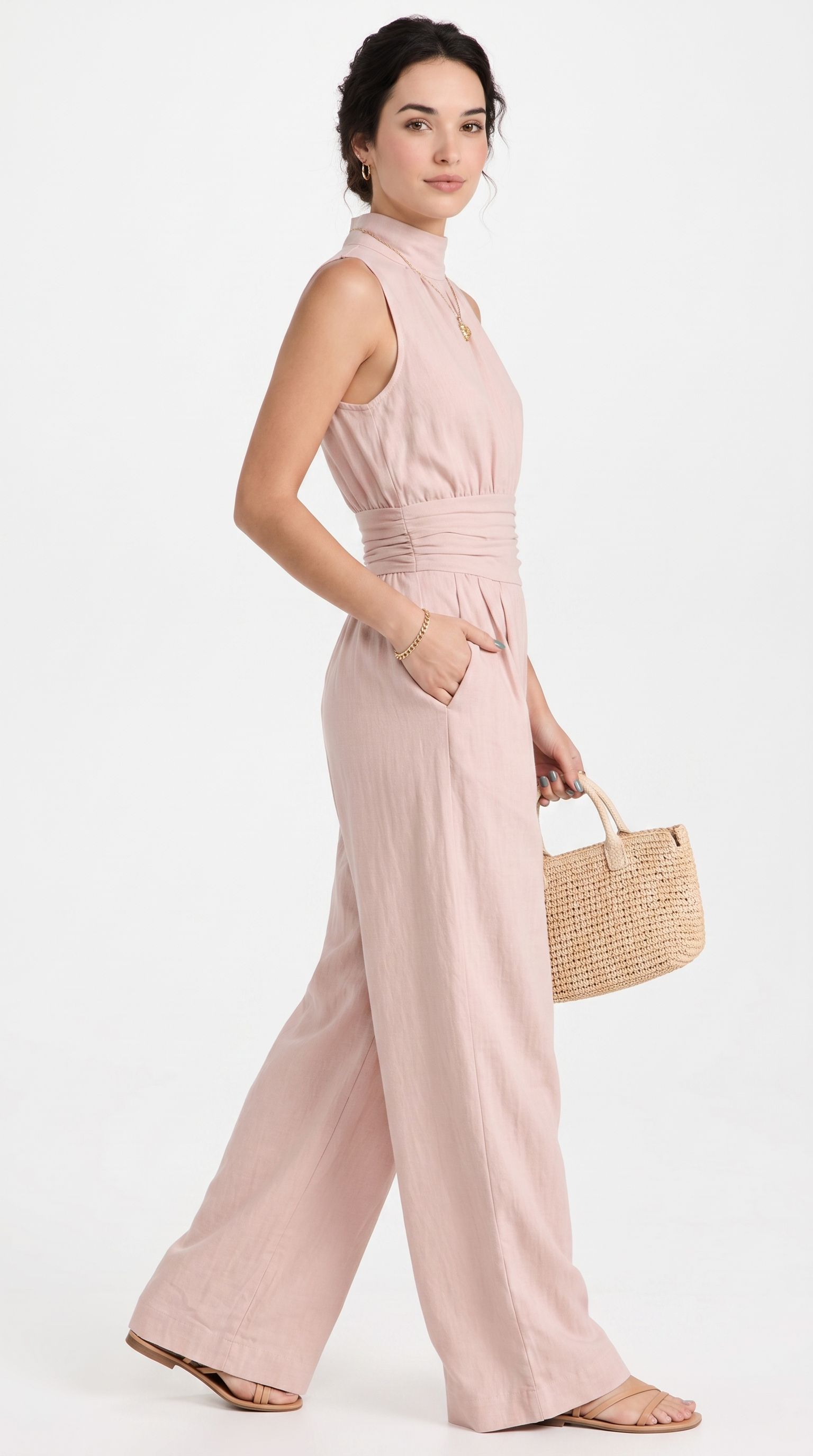 A woman modeling a sleeveless dusty pink wide-leg jumpsuit with a gathered waist, paired with a woven straw handbag and flat sandals, against a plain white studio background, from Meleche Fashion USA or Meléche (short as (Mé))