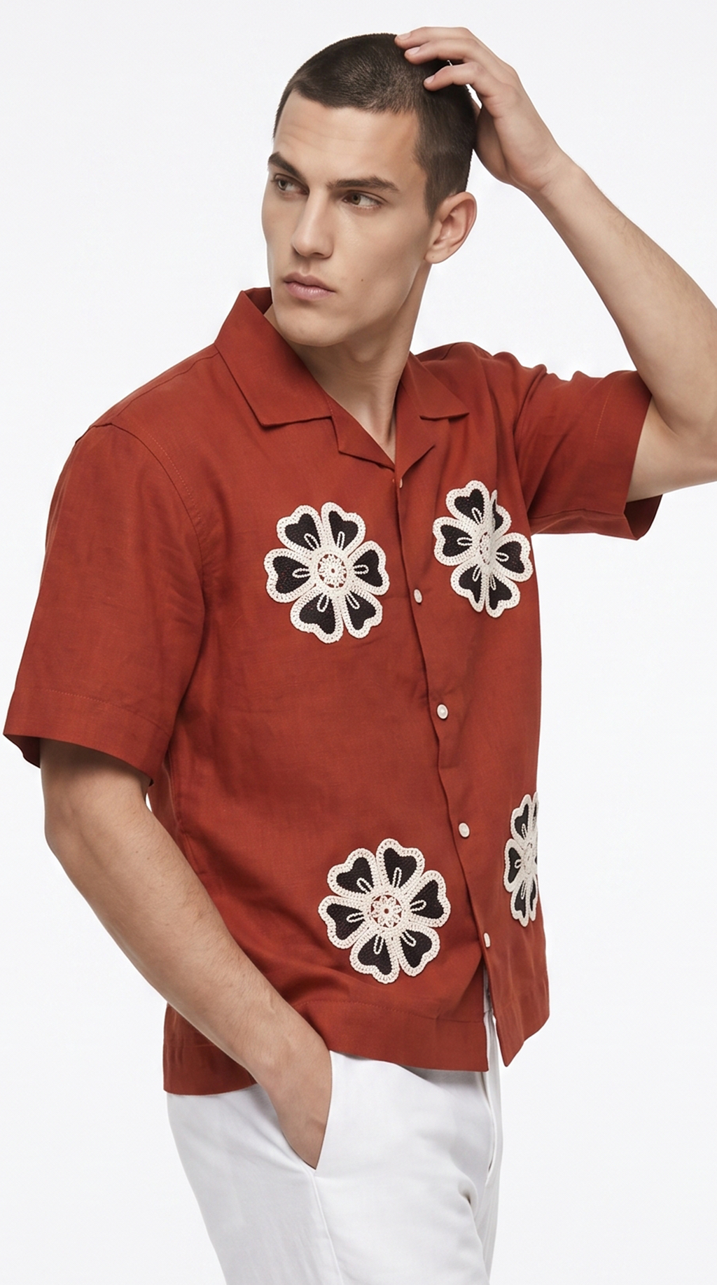 A man wearing a rust-orange short-sleeve button-up shirt with black and white floral embroidery, paired with white pants, against a plain white background, from Meleche Fashion USA or Meléche (short as (Mé))