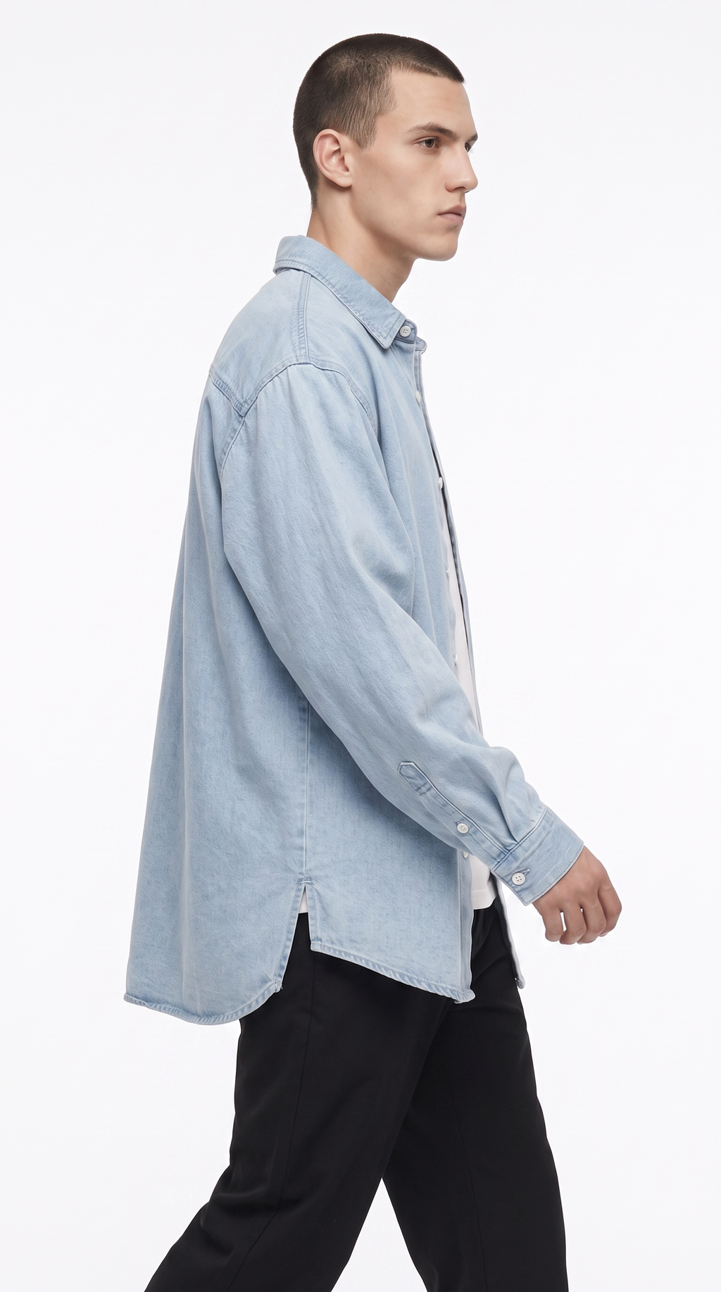 A man in profile wearing an oversized light blue denim shirt over a white undershirt and black pants, photographed against a clean white studio background, from Meleche Fashion USA or Meléche (short as (Mé))