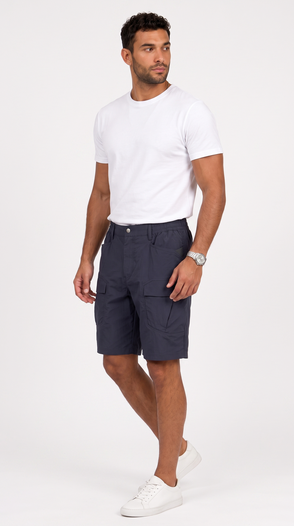 A man wearing a white crewneck t-shirt, navy blue cargo shorts, and white sneakers, standing against a light gray studio background, from Meleche Fashion USA or Meléche (short as (Mé))
