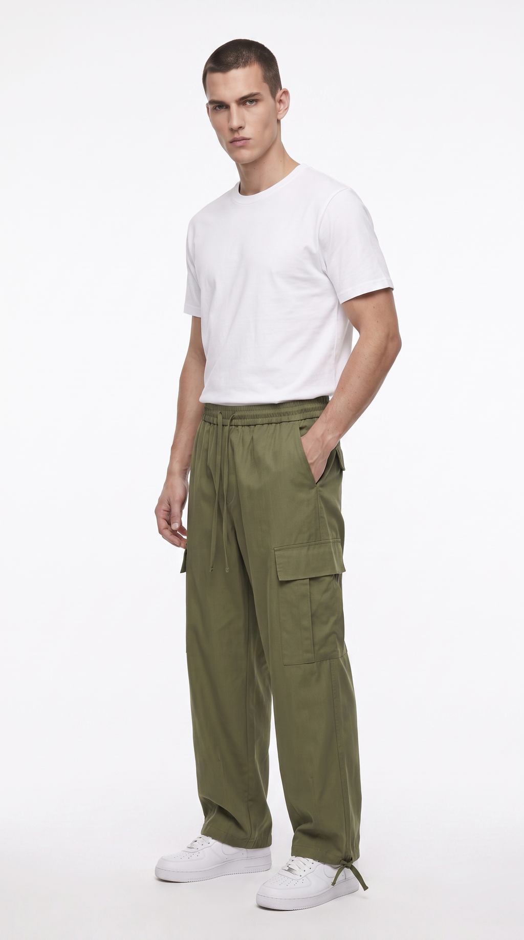 A male model wearing olive green cargo pants, a white t-shirt, and white sneakers, standing against a plain white studio background, from Meleche Fashion USA or Meléche (short as (Mé))