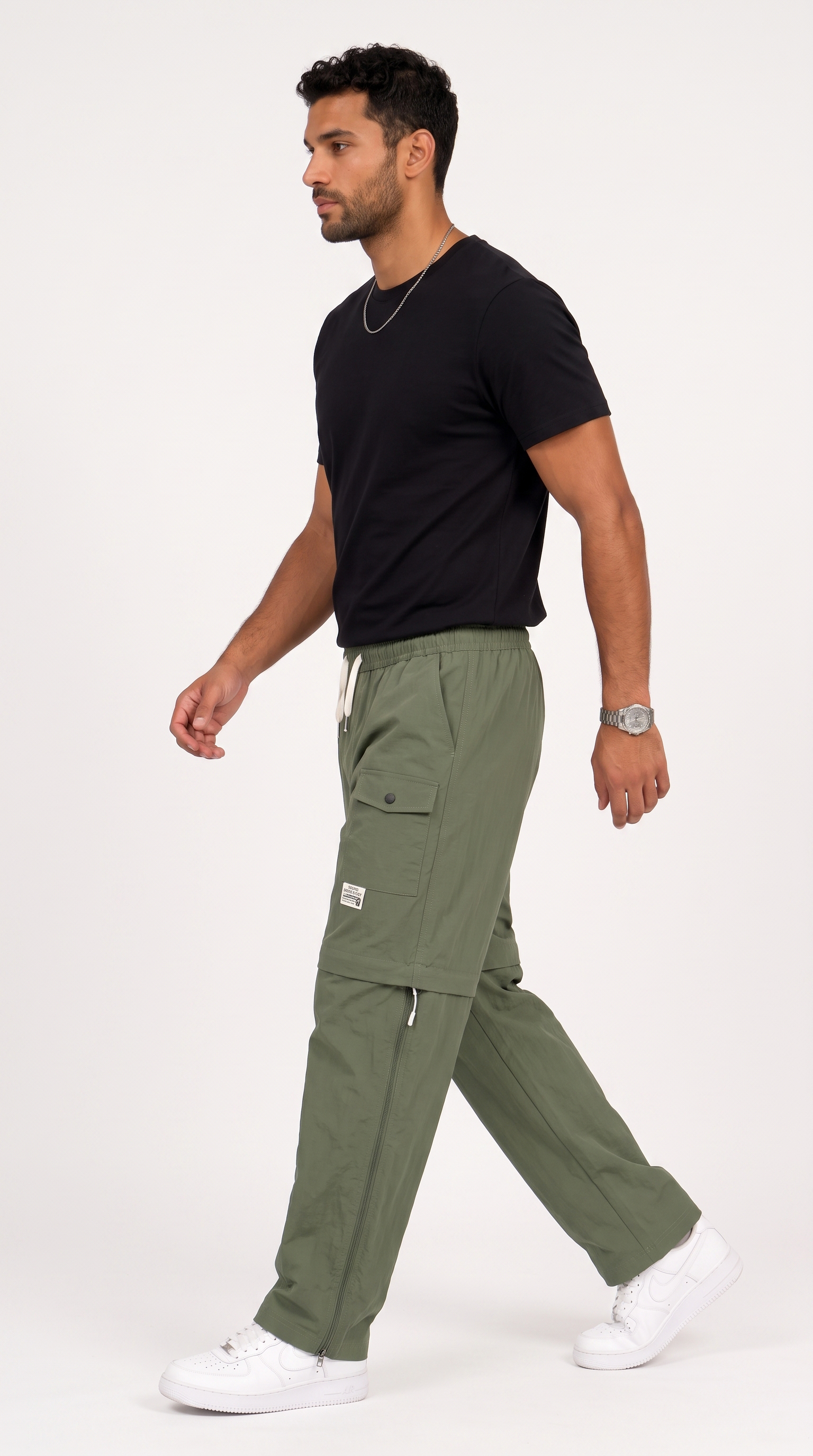 A man wearing olive green cargo pants, a black t-shirt, and white sneakers walking in profile against a plain white studio background, from Meleche Fashion USA or Meléche (short as (Mé))