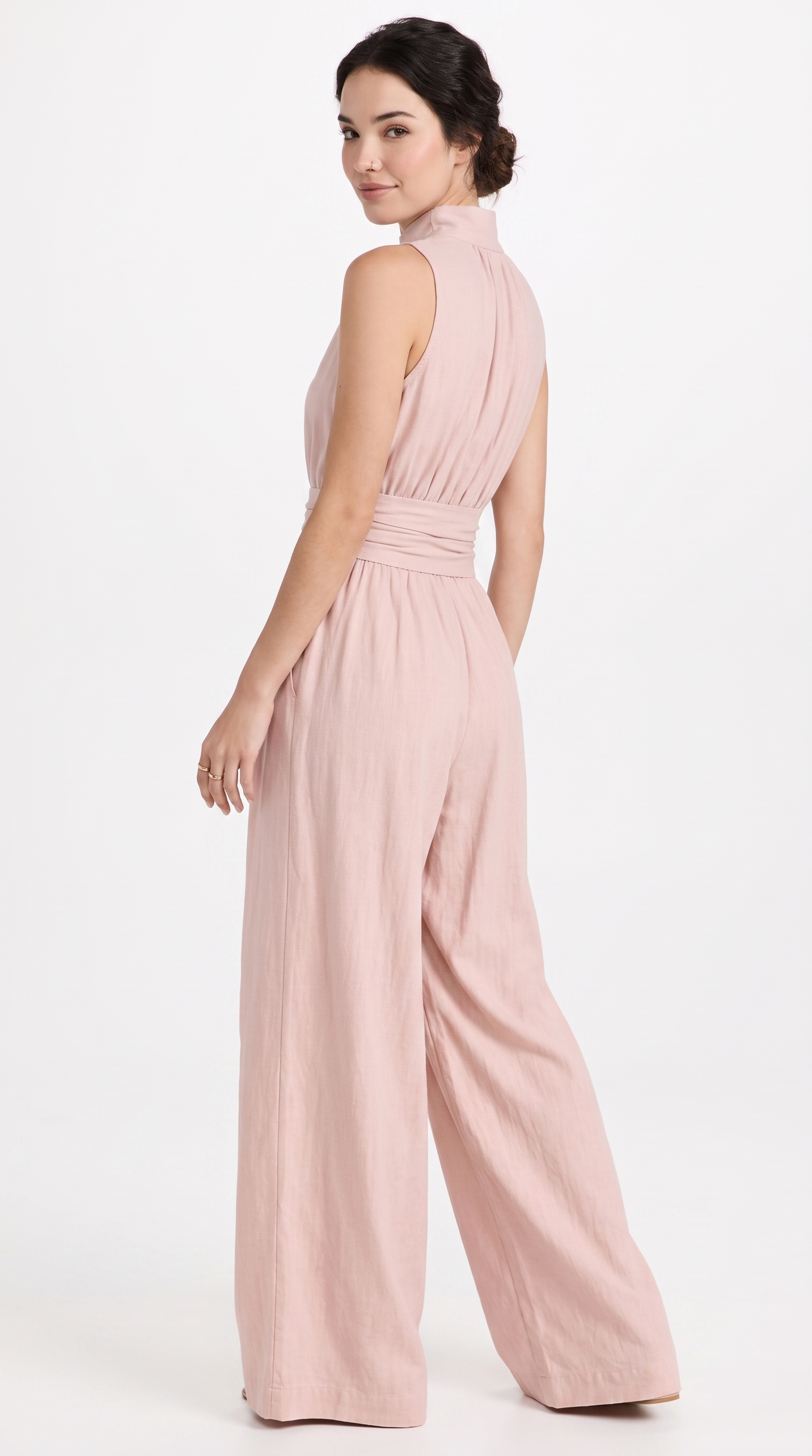 A woman modeling a sleeveless dusty pink wide-leg jumpsuit, shown from a three-quarters back angle against a plain white studio background, from Meleche Fashion USA or Meléche (short as (Mé))