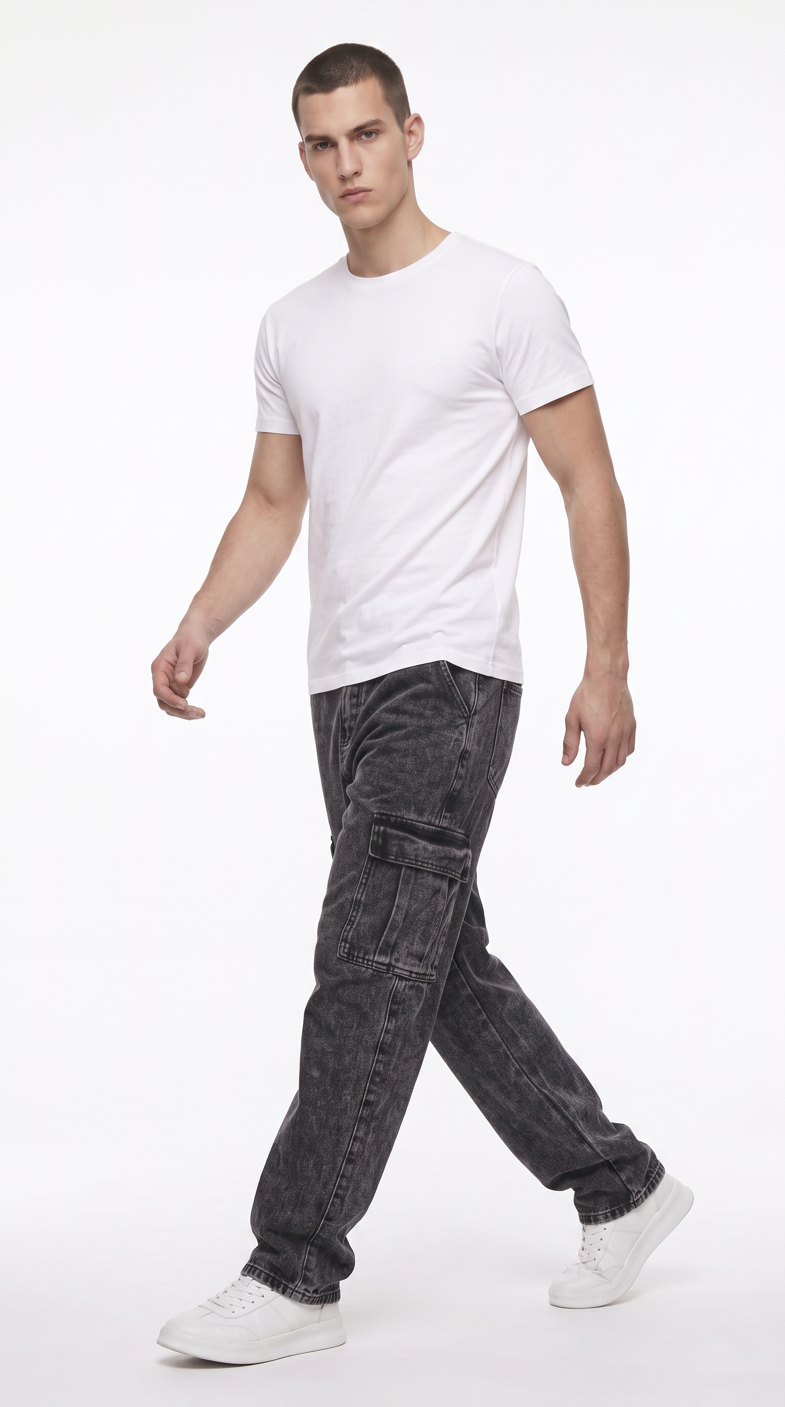 A man modeling a white crew-neck t-shirt and dark gray washed cargo jeans with white sneakers, captured in a side-profile walking pose against a clean white studio background, from Meleche Fashion USA or Meléche (short as (Mé))