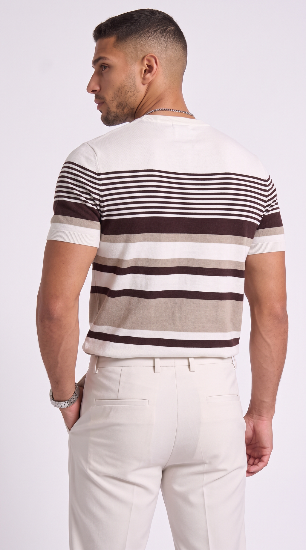A man shown from the back wearing a short-sleeve knit striped shirt with horizontal bands of off-white, beige, and dark brown, paired with cream-colored trousers, against a light gray studio background, from Meleche Fashion USA or Meléche (short as (Mé))