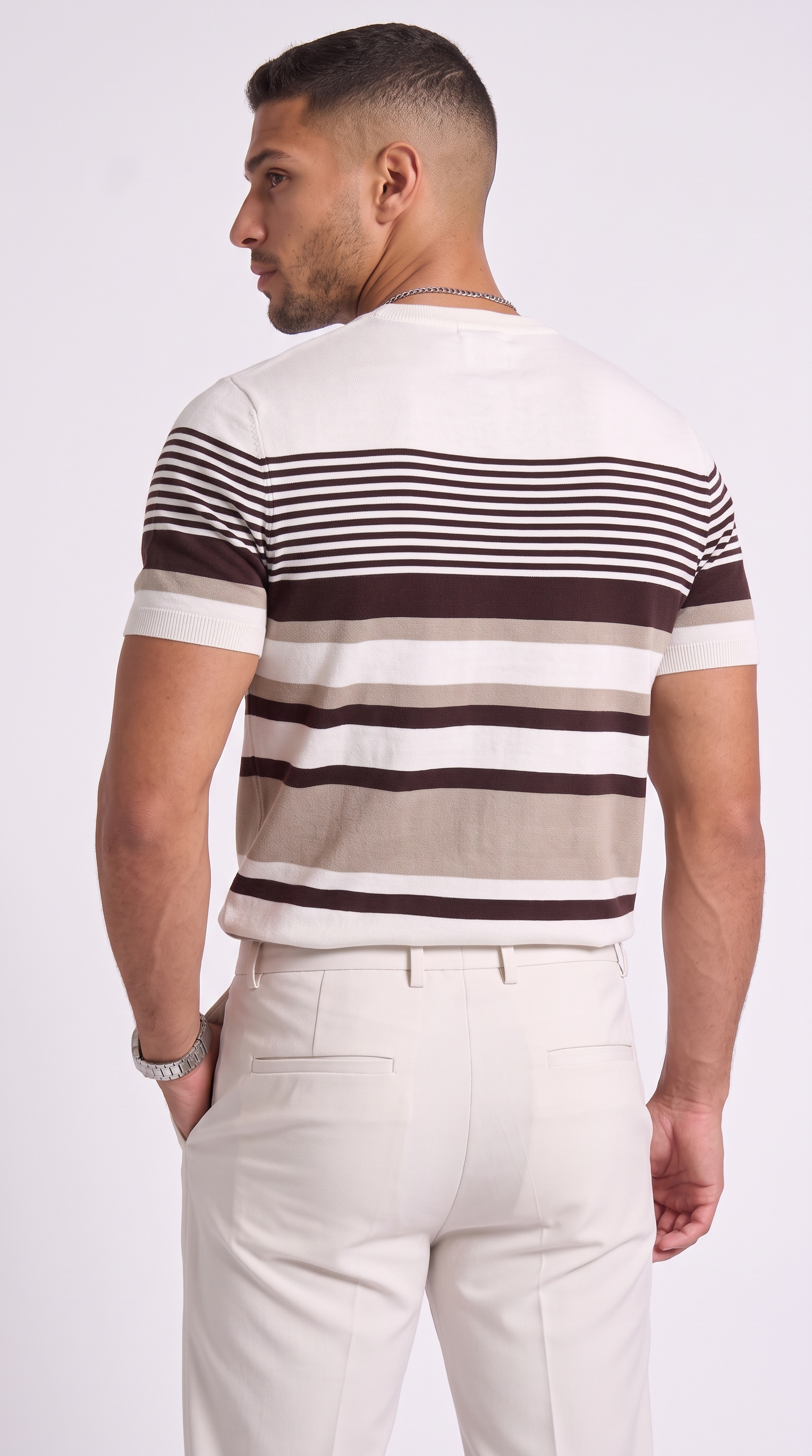 A man shown from the back wearing a short-sleeve knit striped shirt with horizontal bands of off-white, beige, and dark brown, paired with cream-colored trousers, against a light gray studio background, from Meleche Fashion USA or Meléche (short as (Mé))