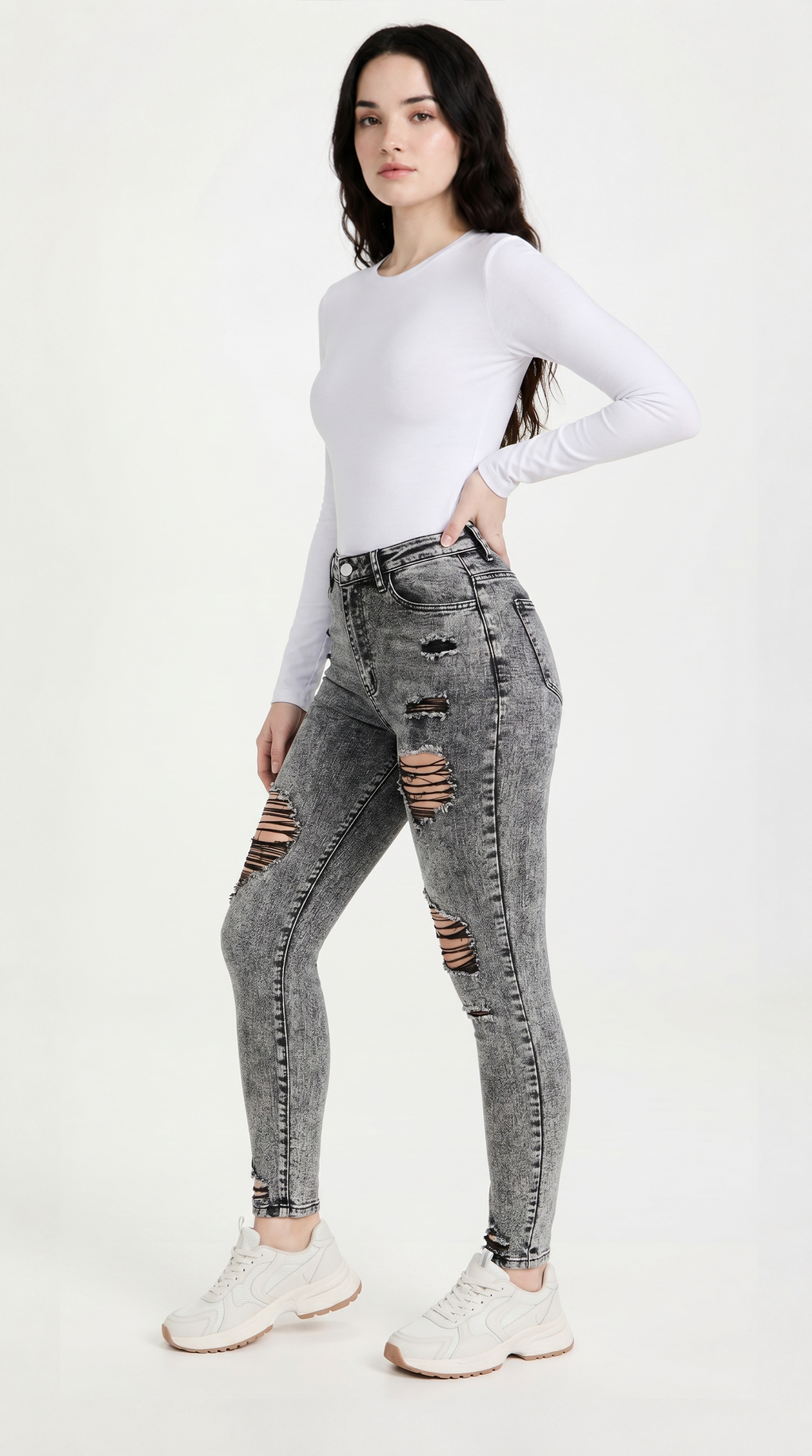 Woman wearing gray distressed jeans and a white long-sleeve top on a white background, slim fit Skinny jeans from Meleche Fashion USA or Meléche (short as (Mé))
