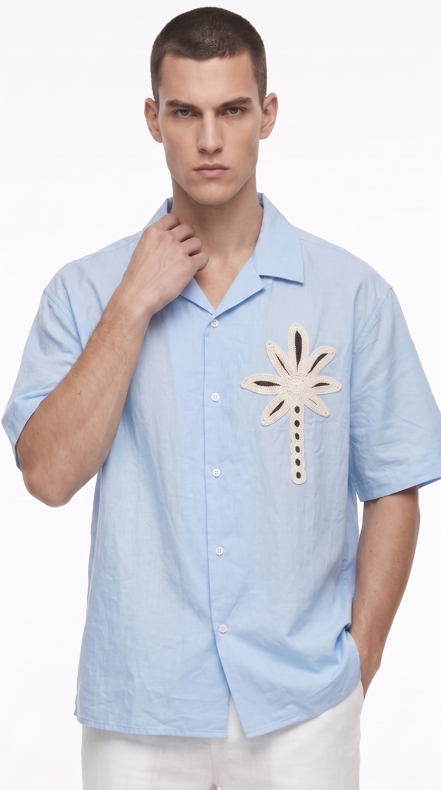 A man wearing a light blue short-sleeve button-up shirt with a beige palm tree embroidery on the chest, paired with white pants, against a plain white background, from Meleche Fashion USA or Meléche (short as (Mé))