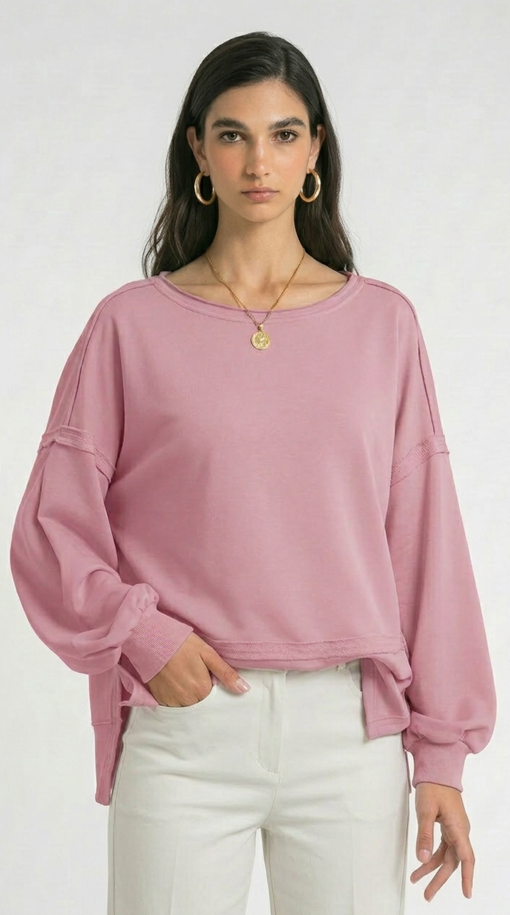Woman wearing a pink sweater and white pants on a white background