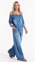A woman modeling a blue denim cold-shoulder jumpsuit with wide legs, button-front chest, and rolled sleeves, photographed against a plain white studio background, from Meleche Fashion USA or Meléche (short as (Mé))