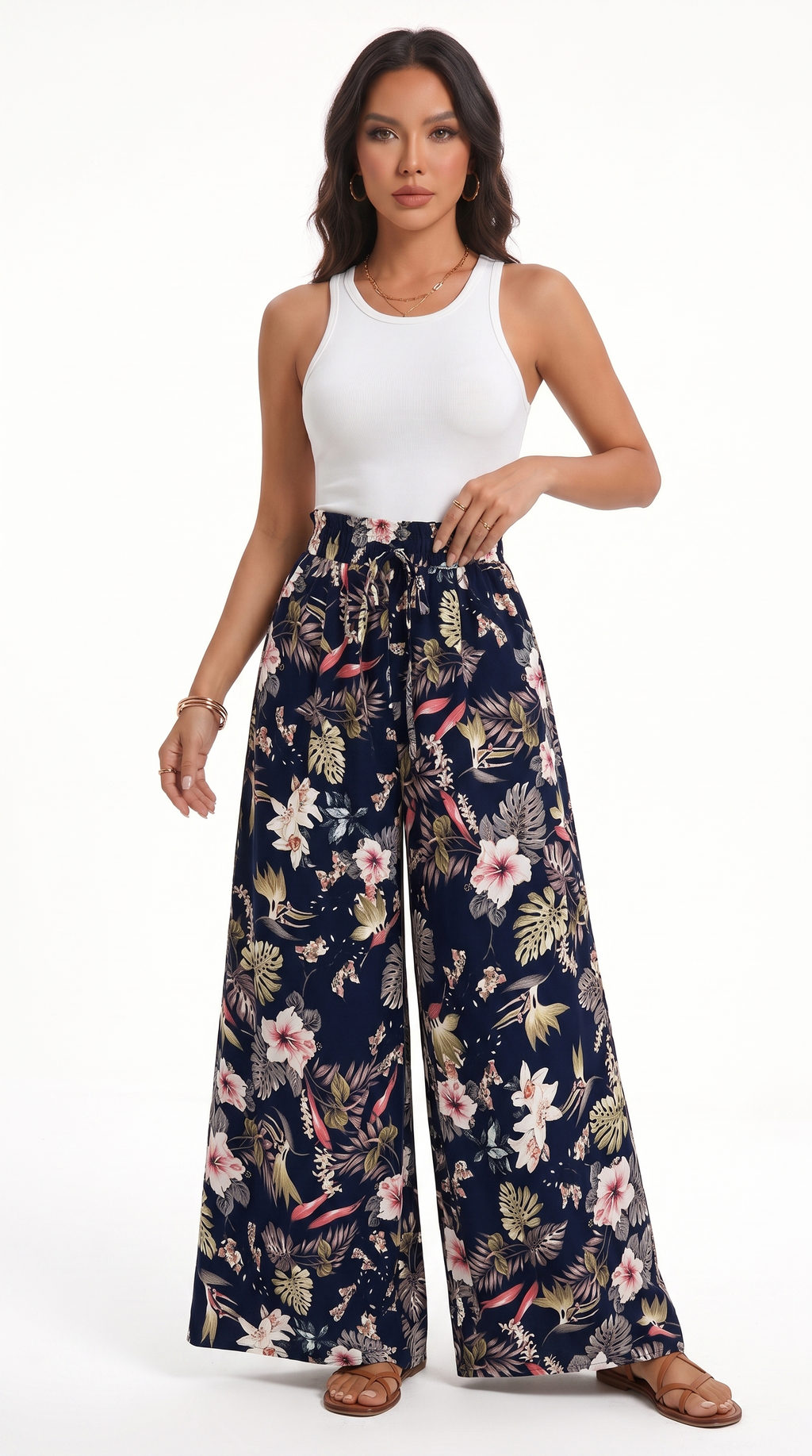 A woman modeling high-waisted, wide-leg pants with a navy blue base and a colorful tropical floral print, paired with a white tank top, against a plain white studio background, from Meleche Fashion USA or Meléche (short as (Mé))