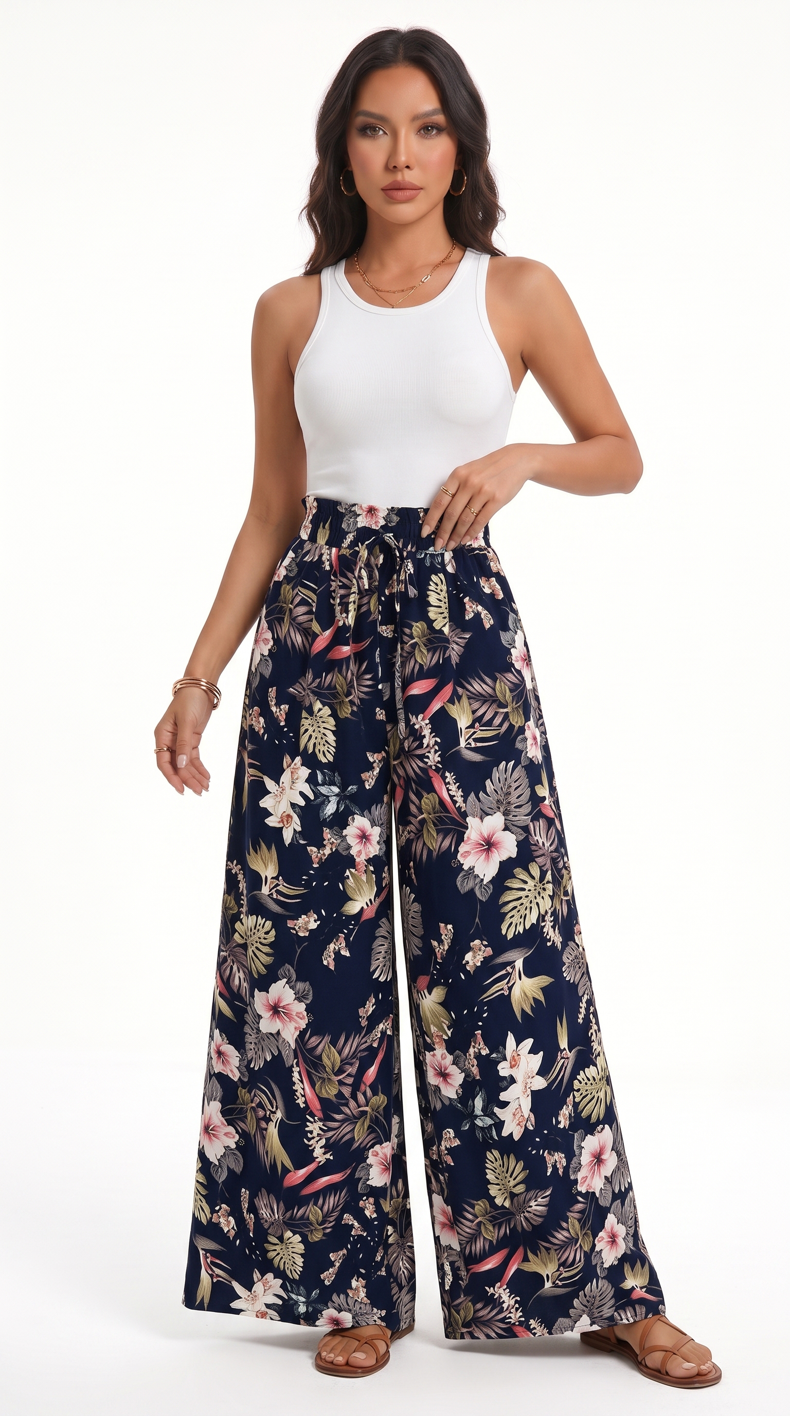 A woman modeling high-waisted, wide-leg pants with a navy blue base and a colorful tropical floral print, paired with a white tank top, against a plain white studio background, from Meleche Fashion USA or Meléche (short as (Mé))