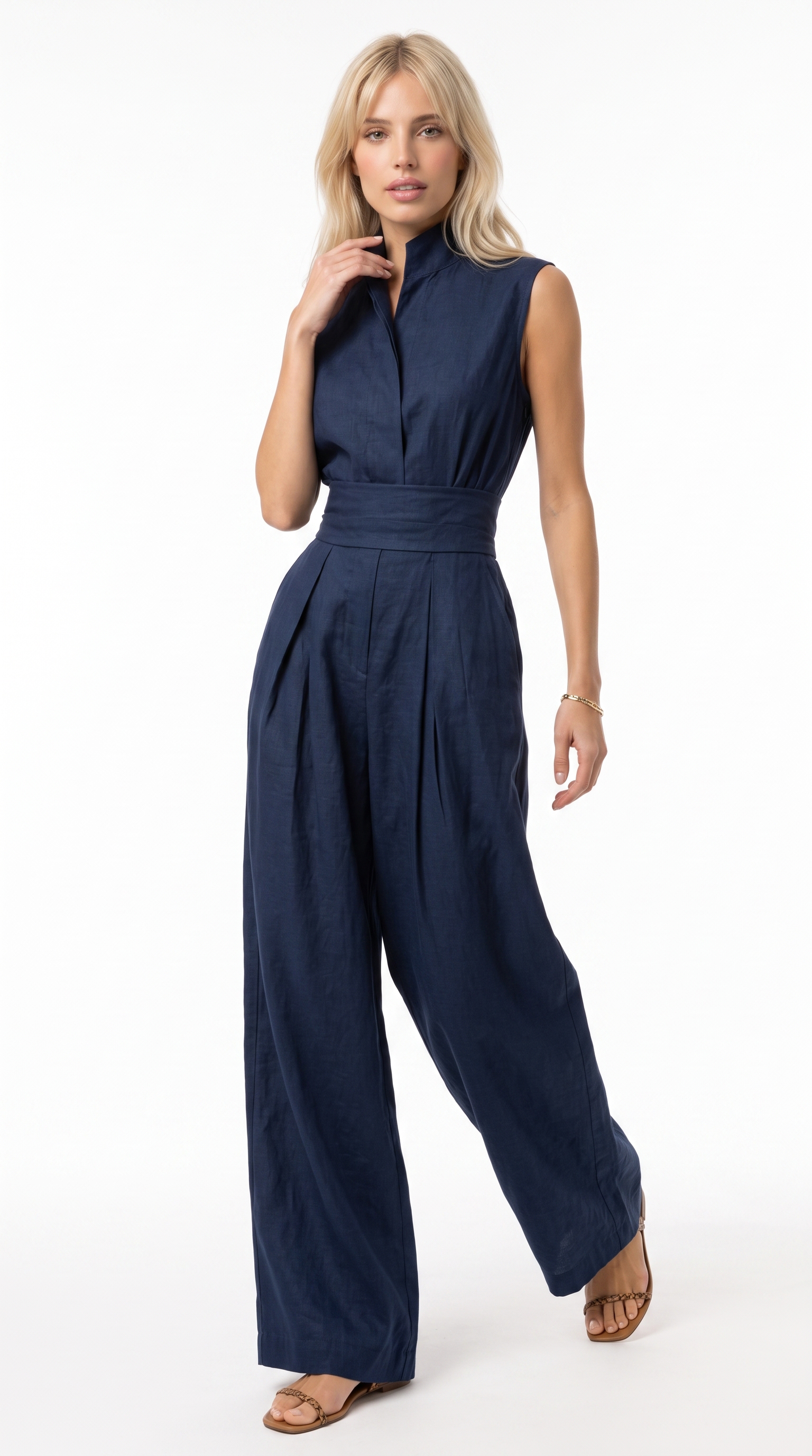 A woman modeling a sleeveless navy blue jumpsuit with a high waist, pleated legs, and a split neckline, photographed against a plain white studio background, from Meleche Fashion USA or Meléche (short as (Mé))