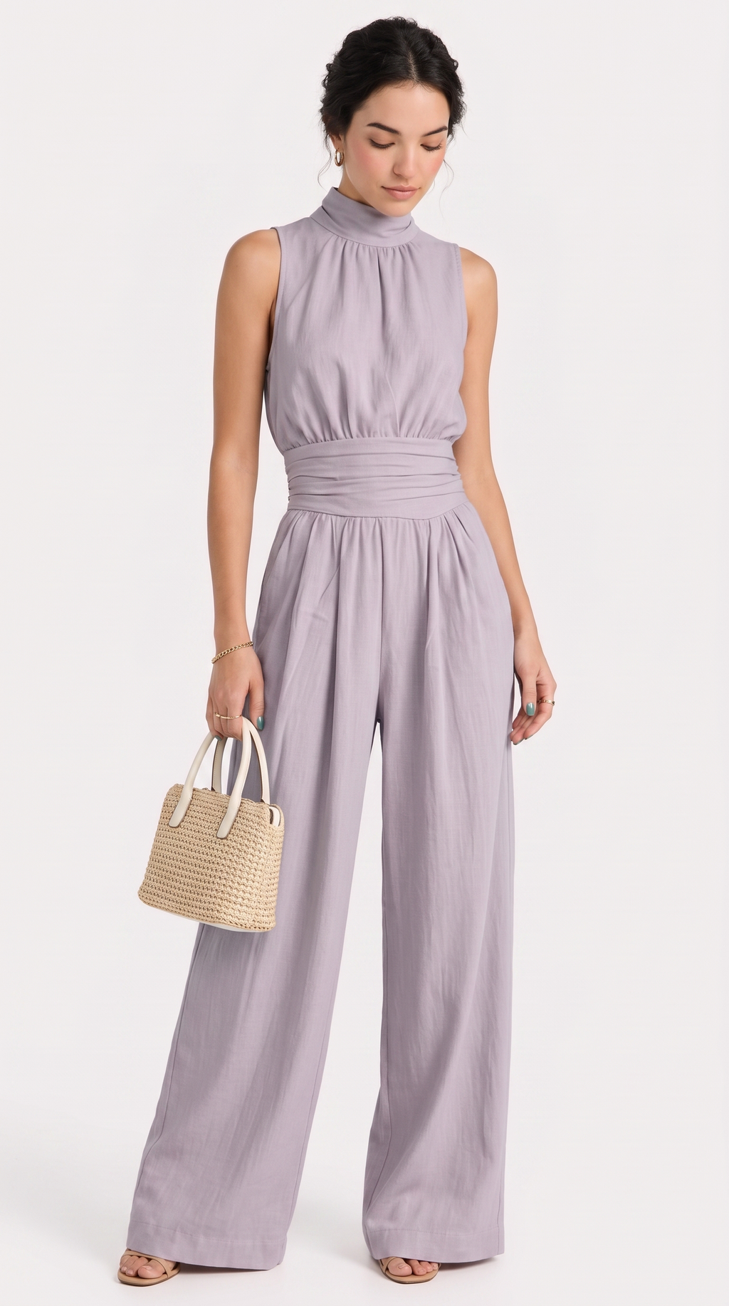 A woman modeling a sleeveless high-neck wide-leg jumpsuit in a dusty lavender-purple color, holding a small woven straw handbag against a clean white studio background, from Meleche Fashion USA or Meléche (short as (Mé))