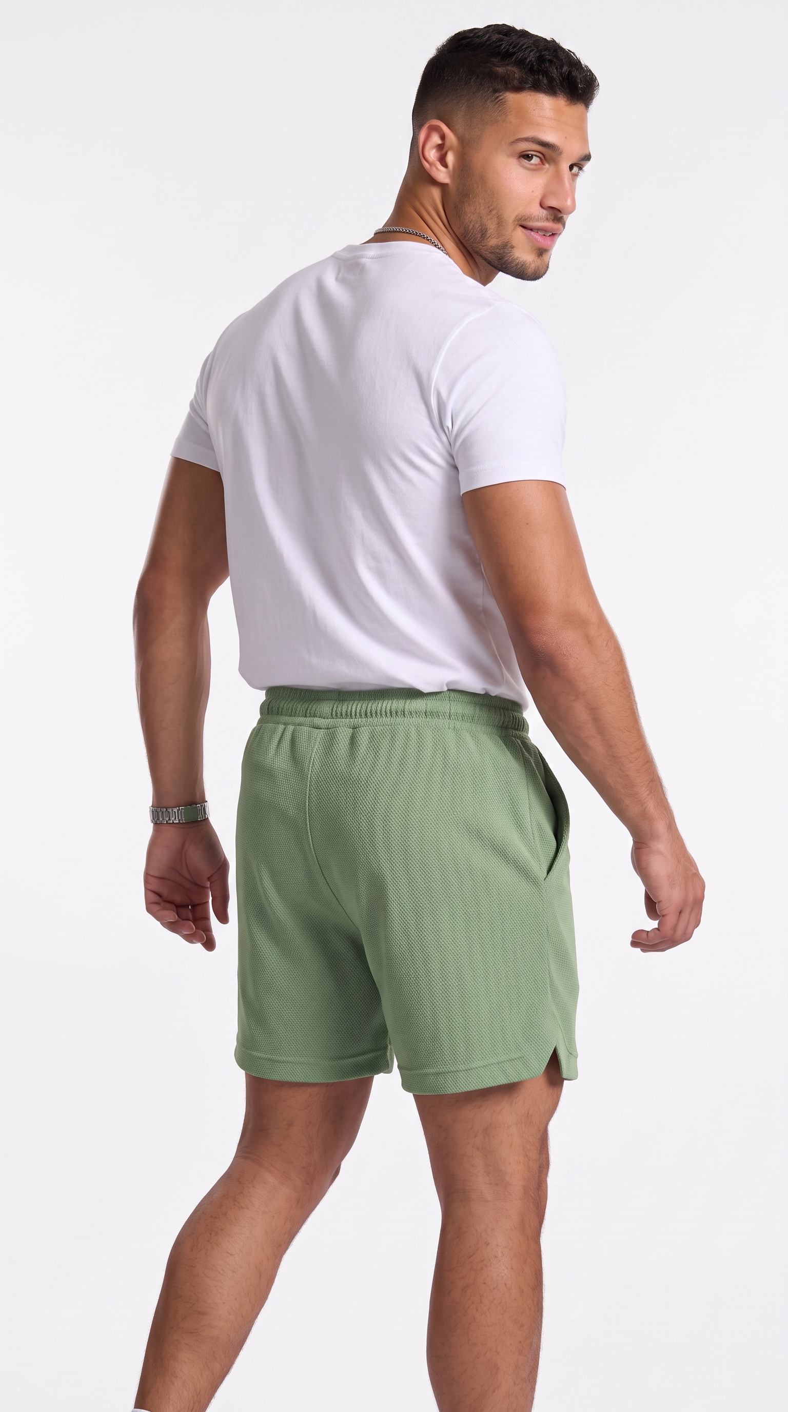 A man wearing sage green athletic shorts and a white t-shirt, shown from a three-quarters back view against a light gray studio background, from Meleche Fashion USA or Meléche (short as (Mé))