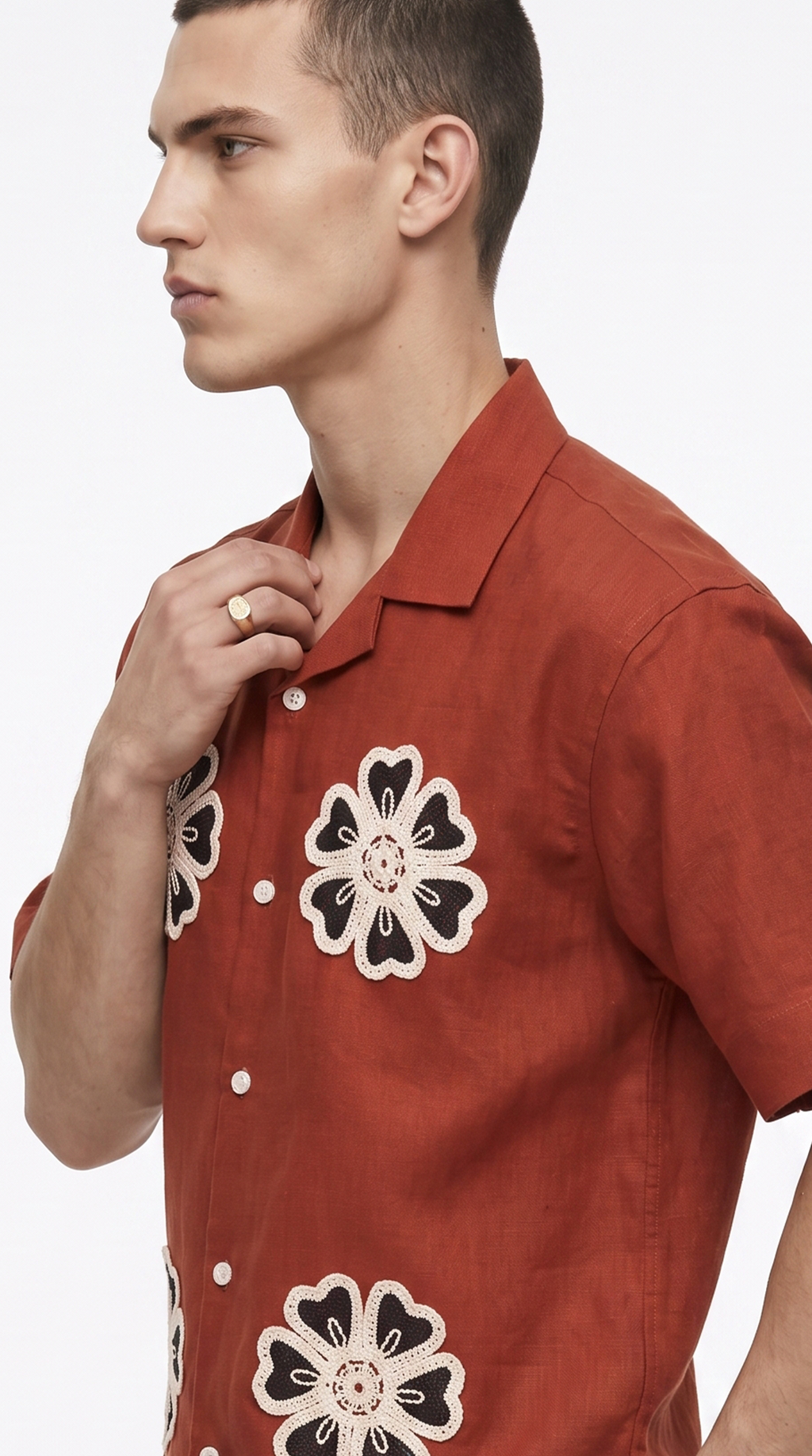 A man in profile wearing a rust-orange short-sleeve button-up shirt with large black and white floral embroidery, photographed against a clean white studio background, from Meleche Fashion USA or Meléche (short as (Mé))