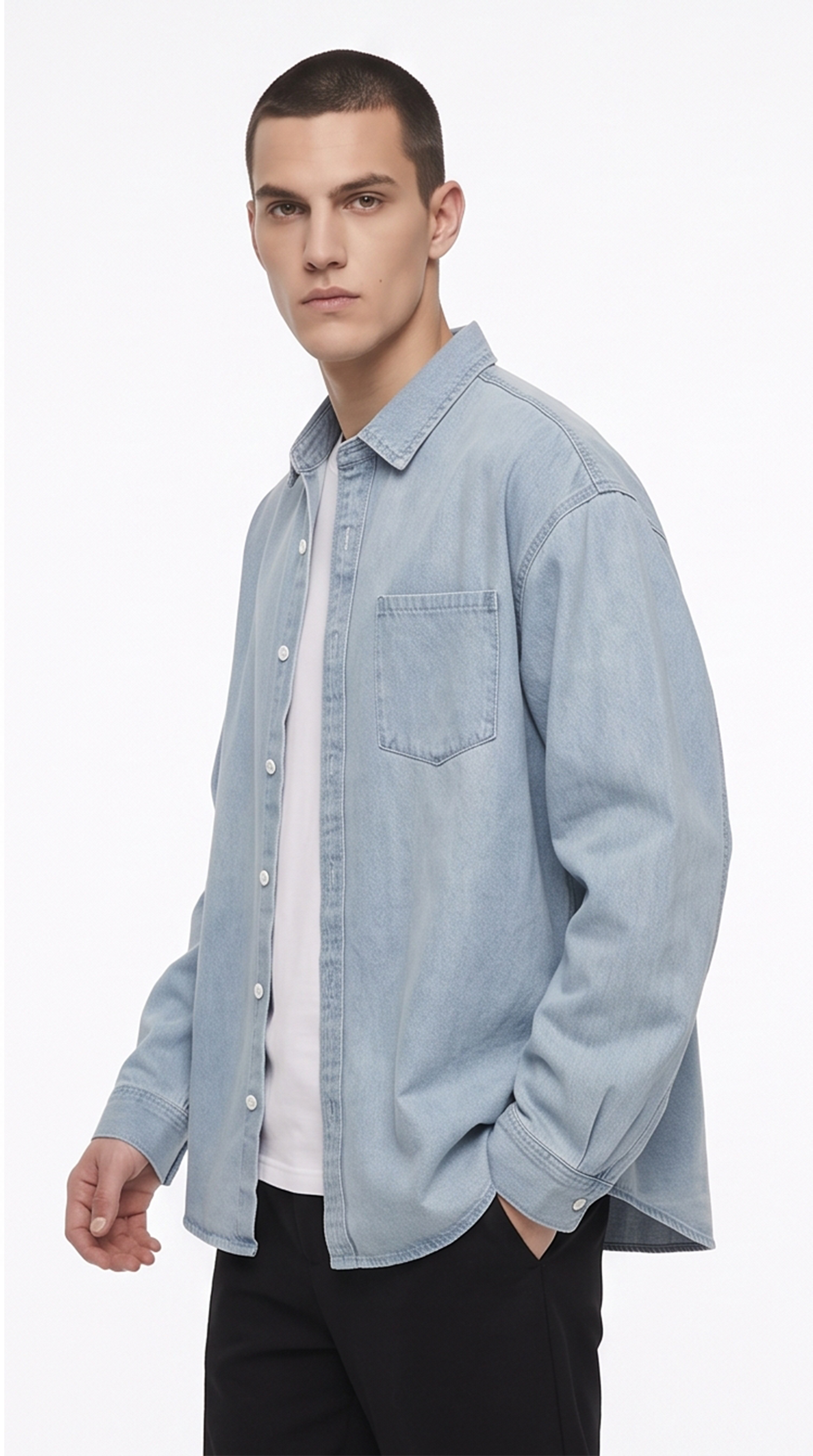 A man wearing a light blue denim button-up shirt over a white t-shirt and black pants, photographed against a plain white studio background, from Meleche Fashion USA or Meléche (short as (Mé))