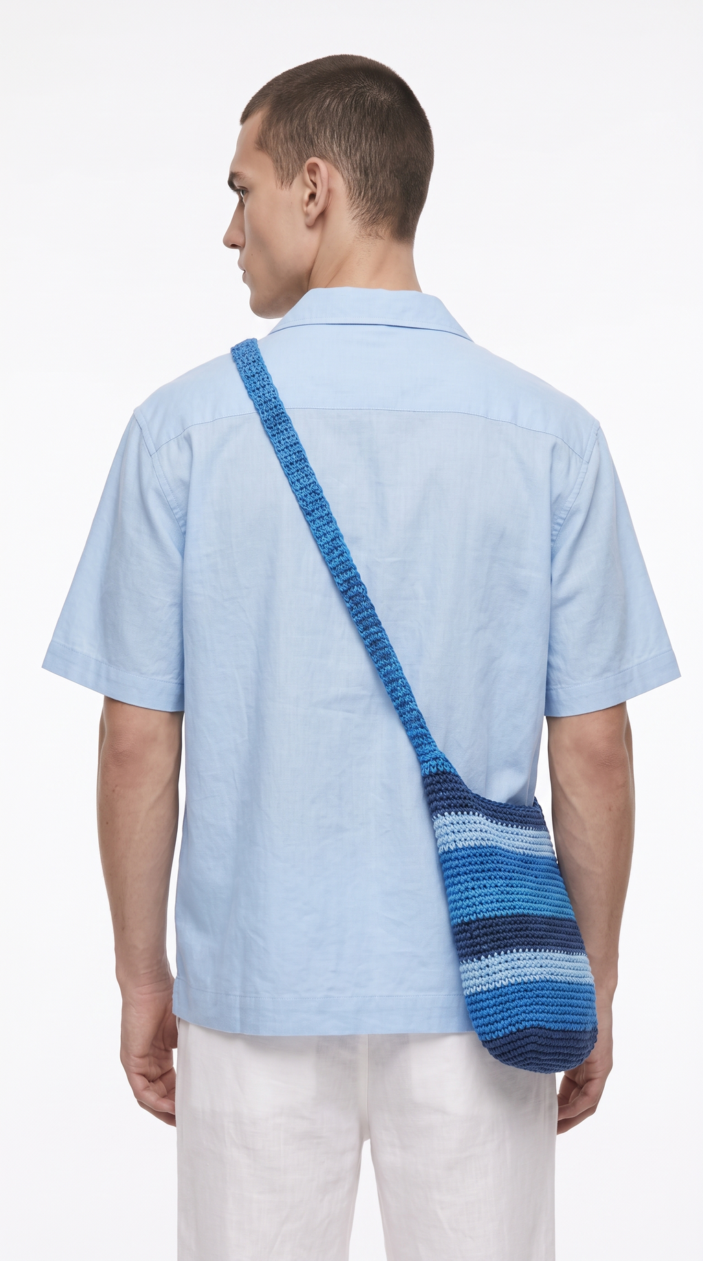 A man viewed from the back wearing a light blue short-sleeve button-up shirt and white pants, with a blue and navy striped shoulder bag slung across his back, from Meleche Fashion USA or Meléche (short as (Mé))