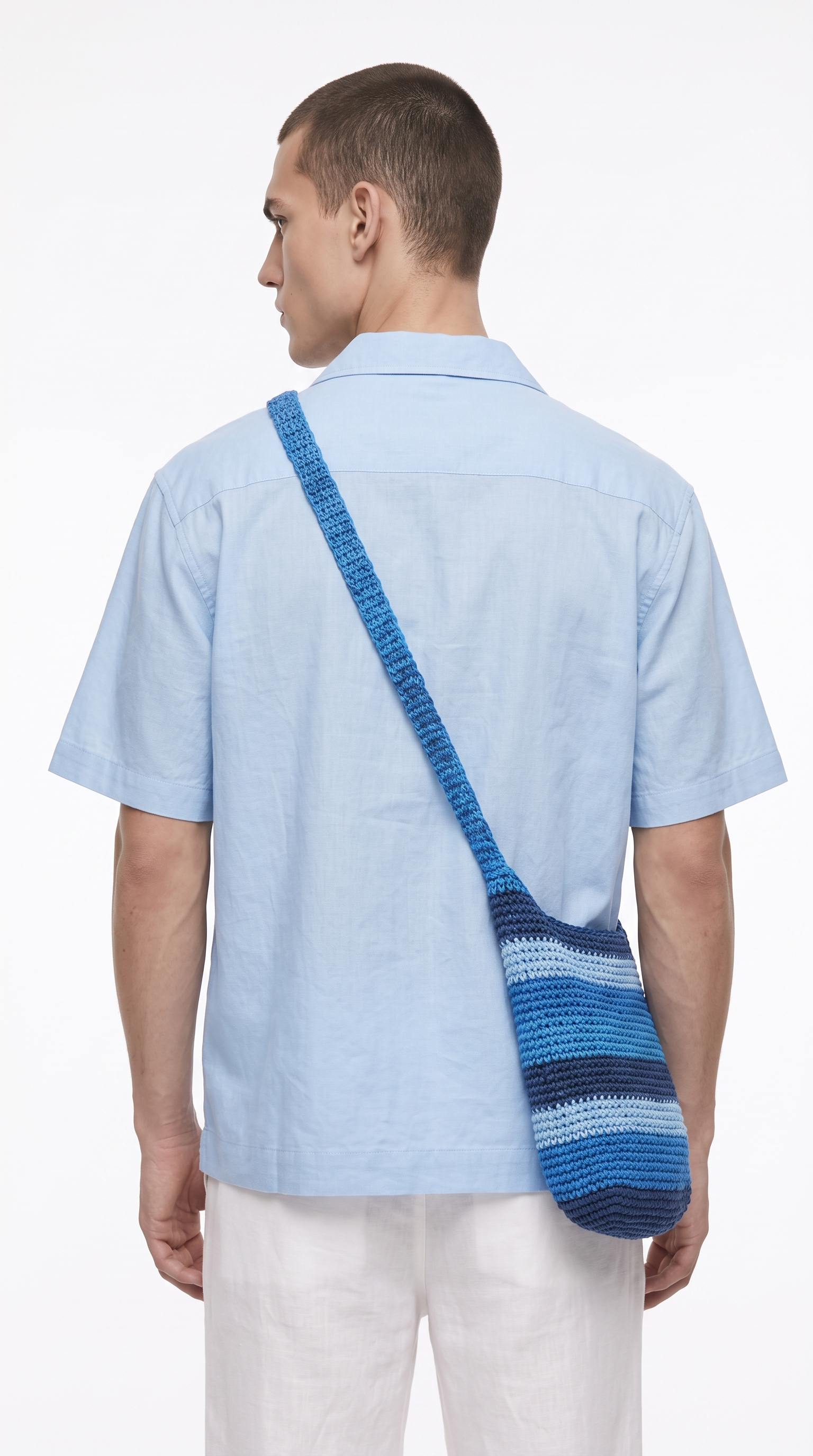 A man viewed from the back wearing a light blue short-sleeve button-up shirt and white pants, with a blue and navy striped shoulder bag slung across his back, from Meleche Fashion USA or Meléche (short as (Mé))
