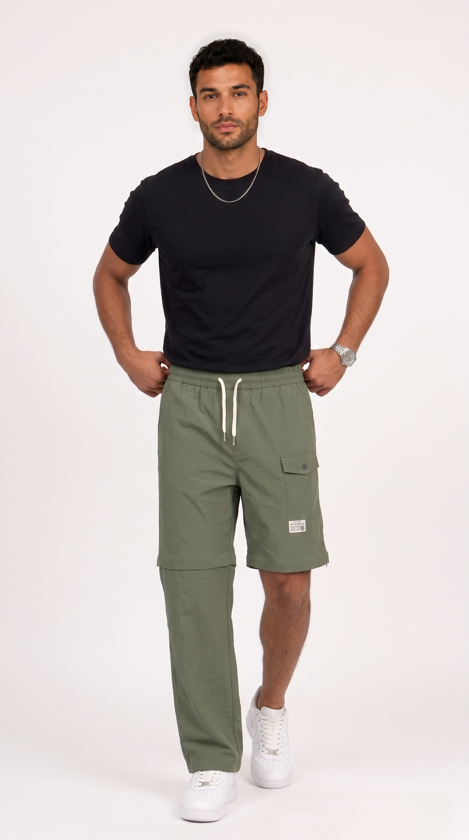 A man modeling olive green cargo shorts with white drawstrings, paired with a black t-shirt and white sneakers, standing against a plain white studio background, from Meleche Fashion USA or Meléche (short as (Mé))