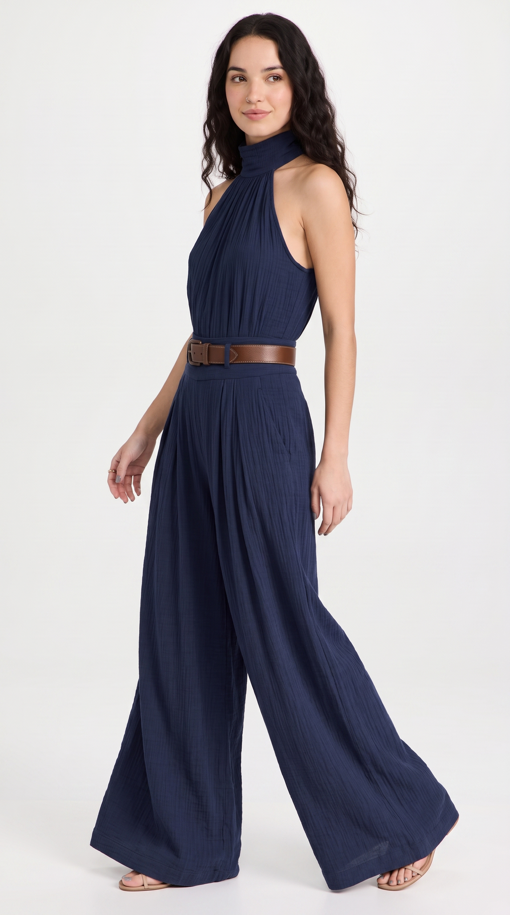 A woman modeling a navy blue halter-neck wide-leg jumpsuit with a brown belt, photographed against a plain white studio background, from Meleche Fashion USA or Meléche (short as (Mé))