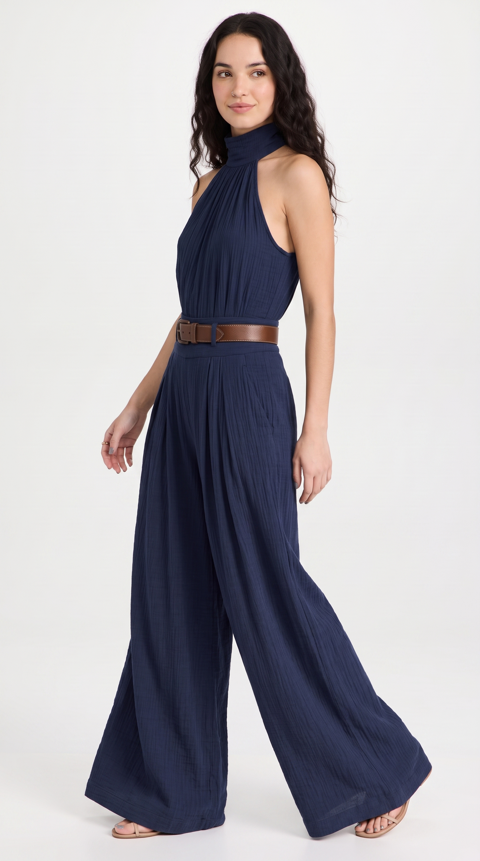 A woman modeling a navy blue halter-neck wide-leg jumpsuit with a brown belt, photographed against a plain white studio background, from Meleche Fashion USA or Meléche (short as (Mé))