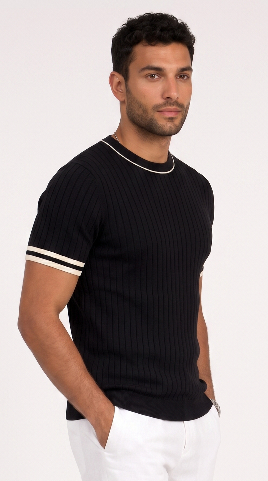 A man wearing a black ribbed short-sleeve crewneck sweater with white contrast trim on the collar and sleeve cuffs, paired with white pants, against a plain white studio background, from Meleche Fashion USA or Meléche (short as (Mé))