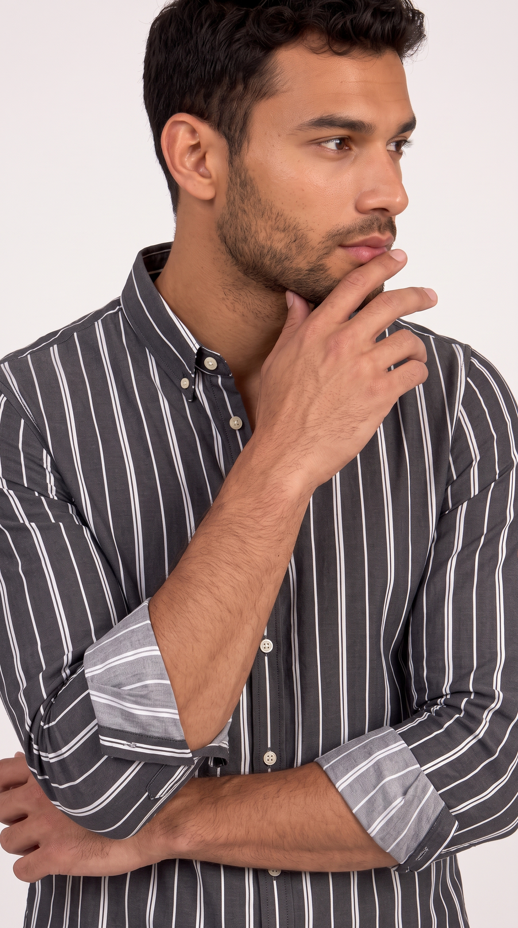 A man wearing a dark gray and white vertically striped button-down shirt, posing with his hand on his chin against a plain light background, from Meleche Fashion USA or Meléche (short as (Mé))