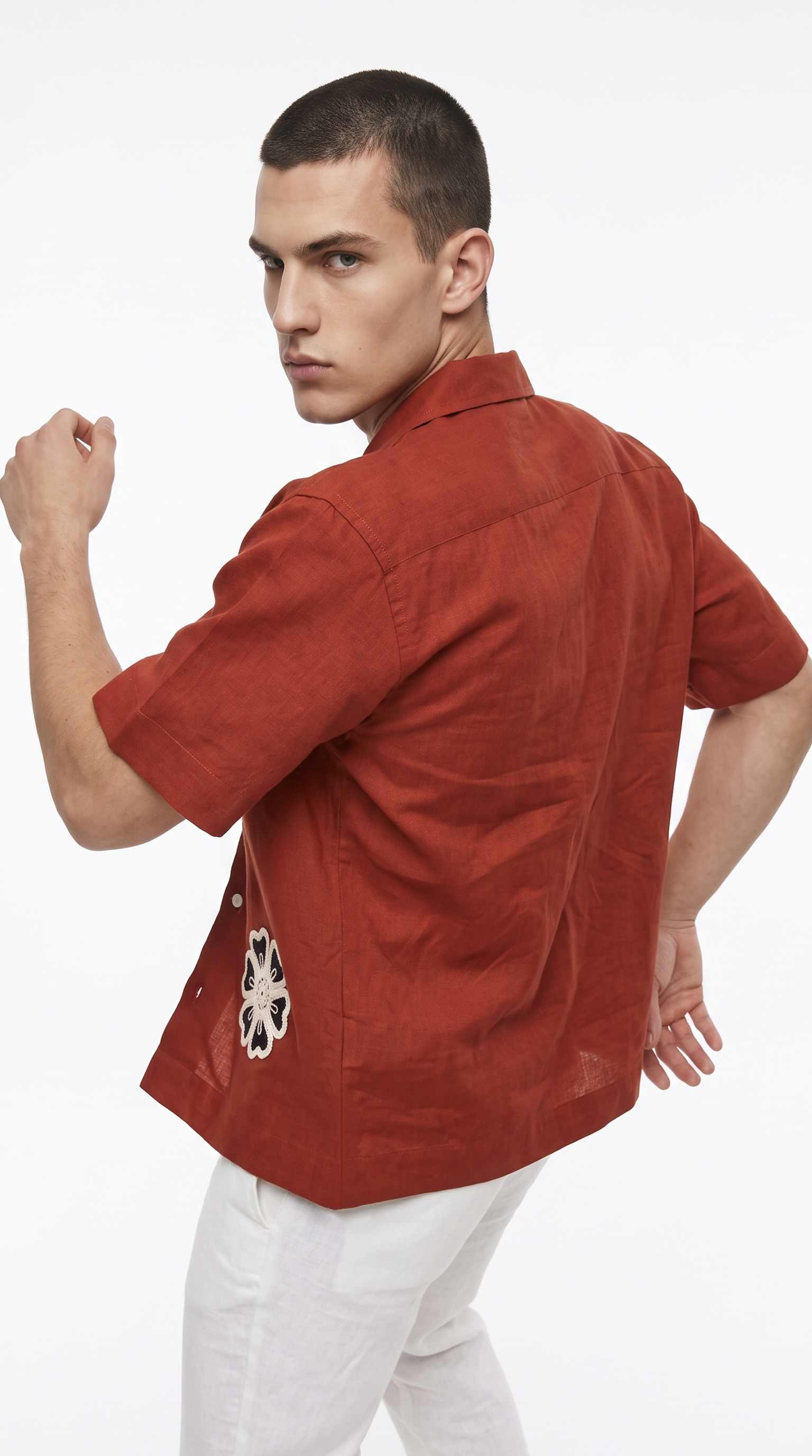 A man wearing a rust-orange short-sleeve button-up shirt with a white and black geometric pattern on the back hem, paired with white pants, photographed against a solid white background, from Meleche Fashion USA or Meléche (short as (Mé))