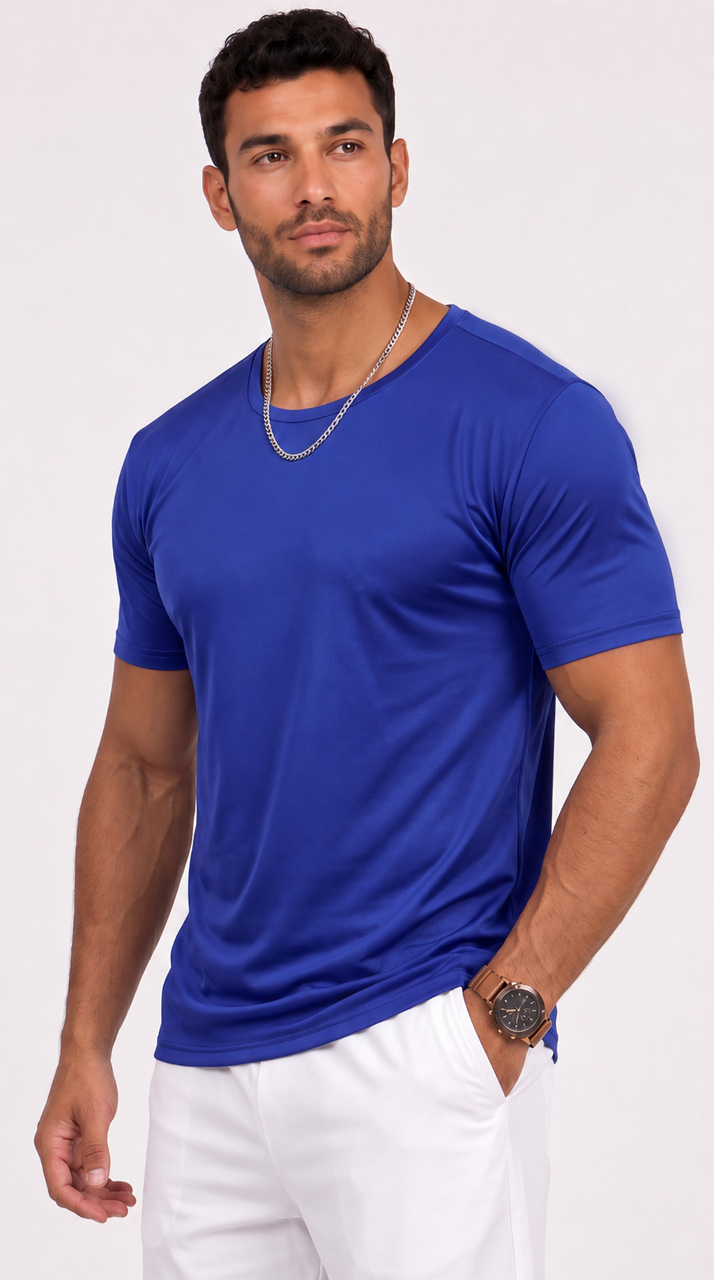 A muscular man wearing a vibrant royal blue short-sleeve crewneck t-shirt and white pants, standing against a plain white studio background, from Meleche Fashion USA or Meléche (short as (Mé))