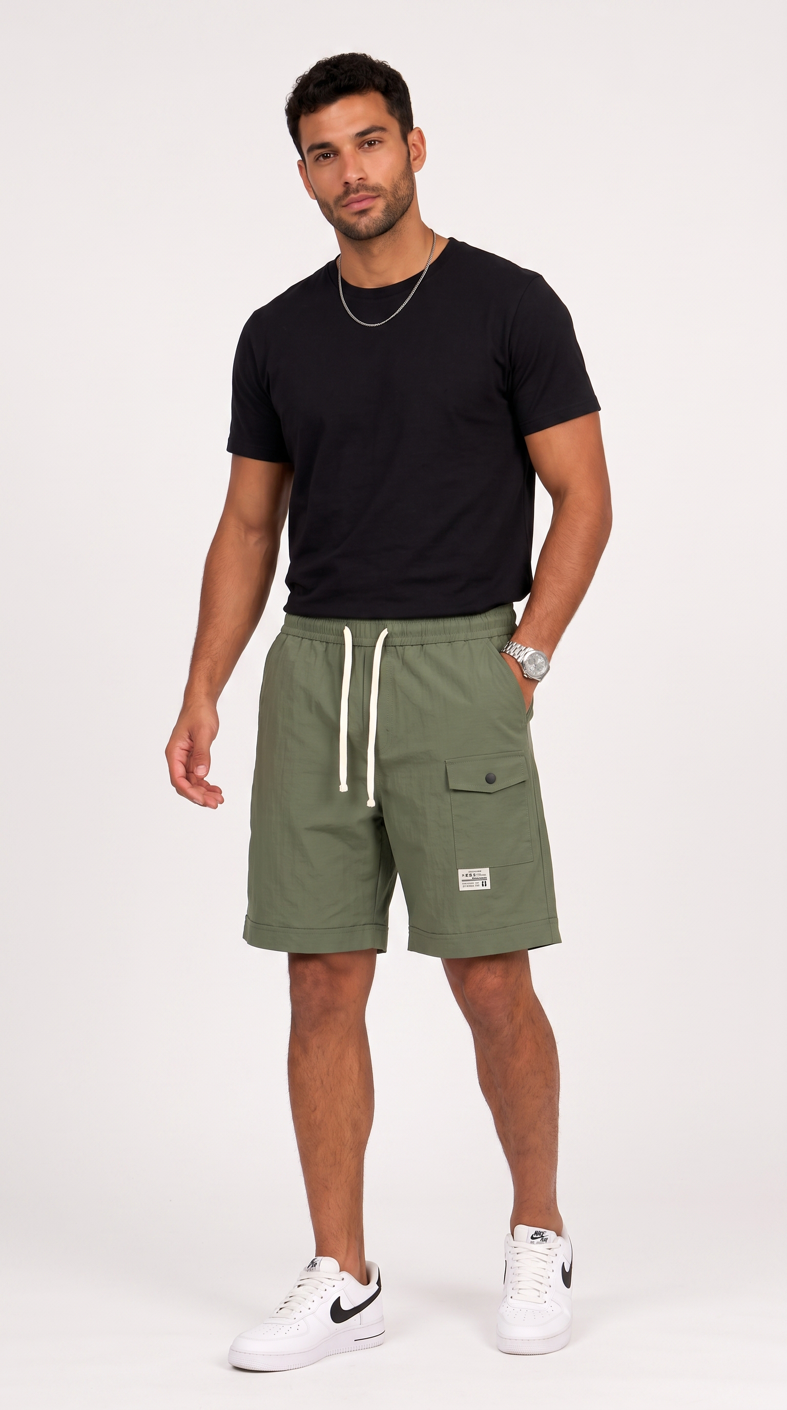 A man modeling olive green cargo shorts with white drawstrings, paired with a black t-shirt and white sneakers, standing against a light gray studio background, from Meleche Fashion USA or Meléche (short as (Mé))